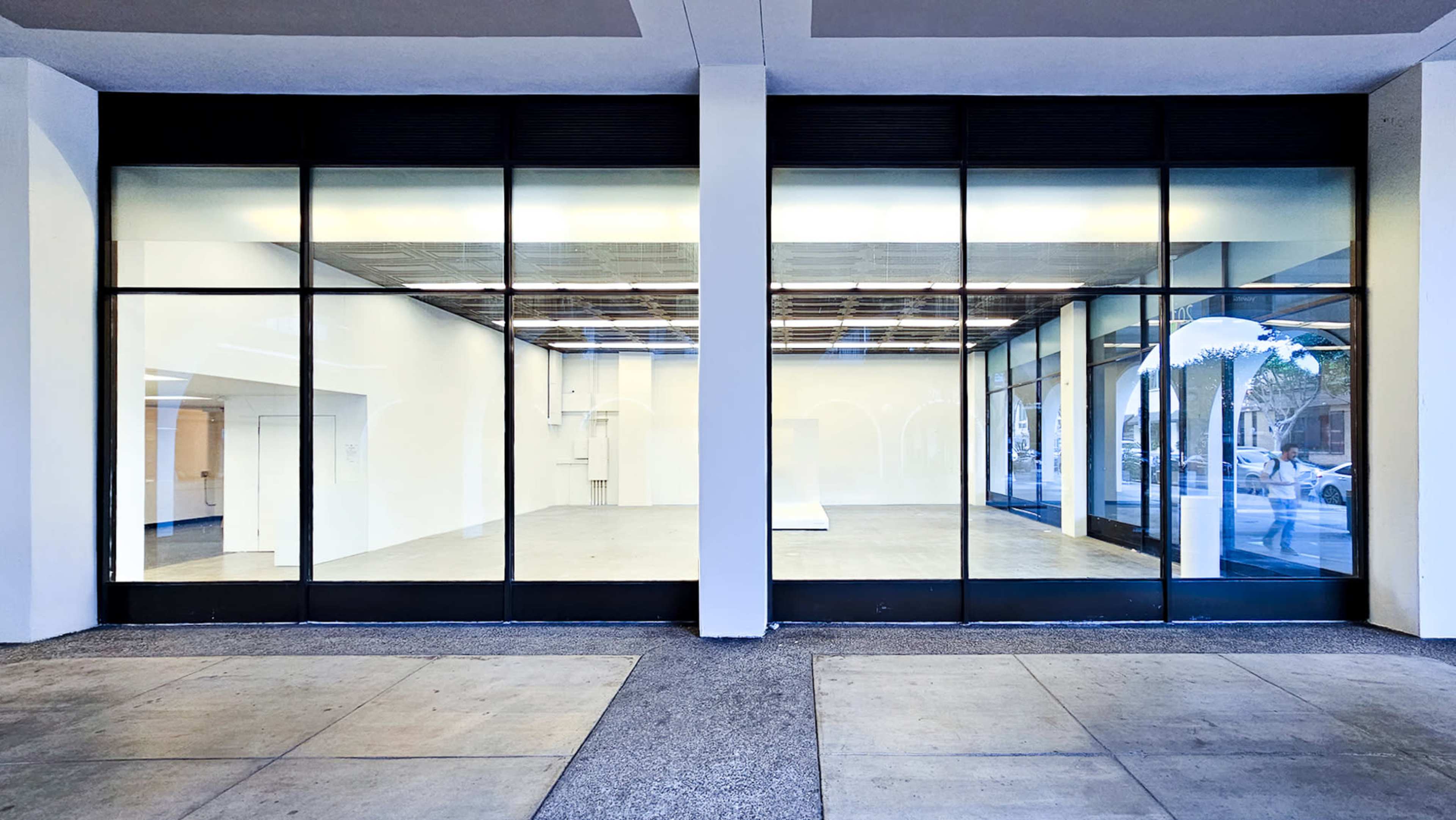 A large commercial space with floor-to-ceiling glass windows showcases an empty interior with white walls and a concrete floor.