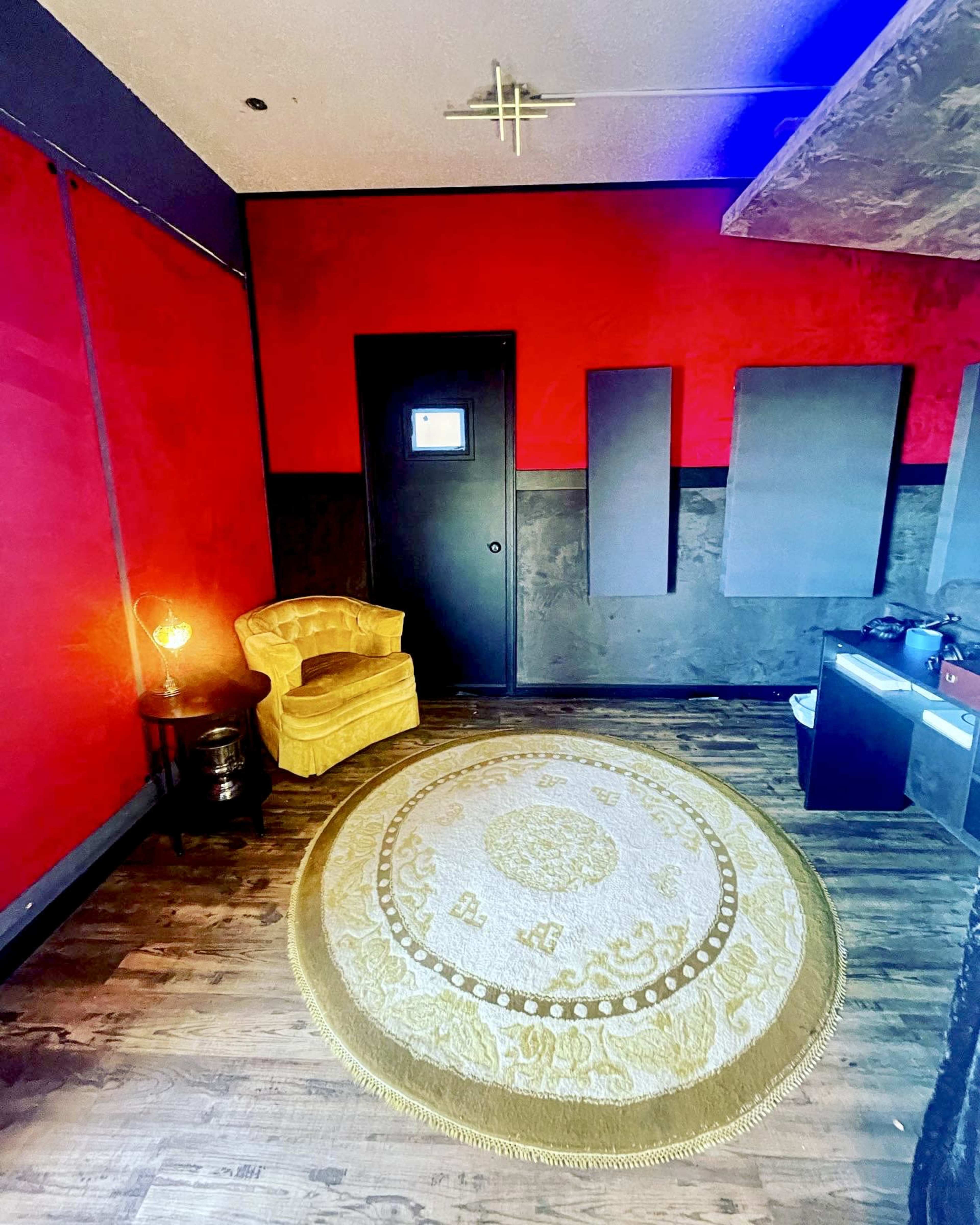 A room with red walls, a wooden floor, a circular rug, a yellow armchair, and a closed black door.