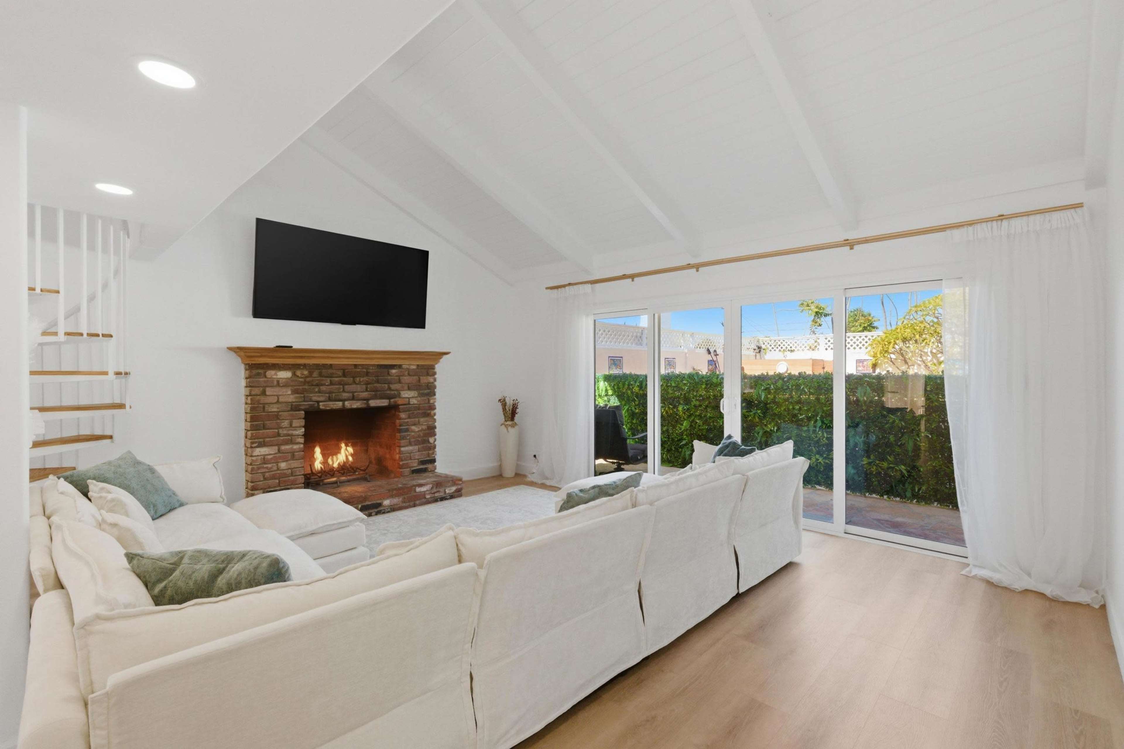 A cozy living room features a fireplace with a brick surround, a large sectional sofa, and sliding glass doors leading to an outdoor area.