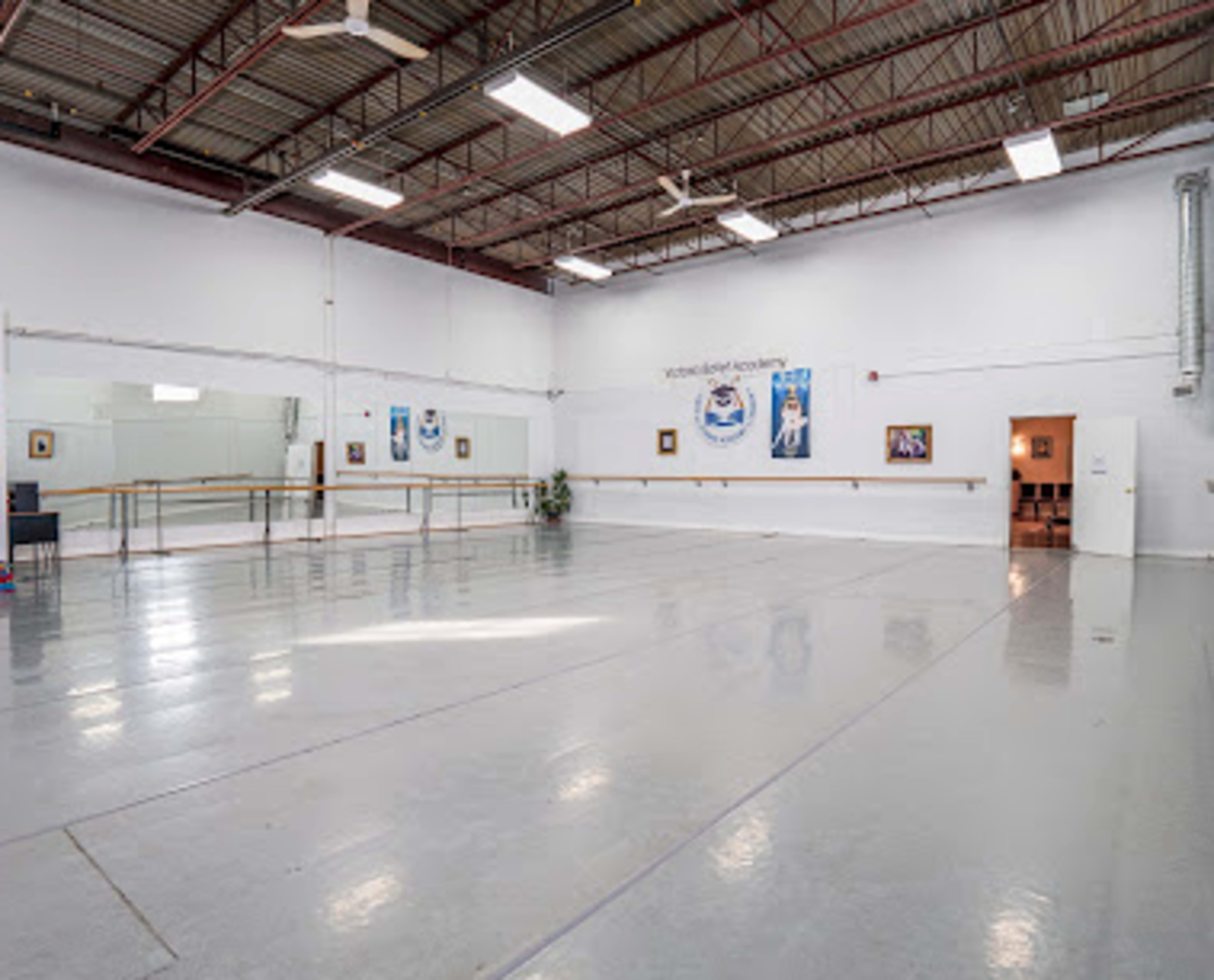 A spacious dance studio with mirrors along one wall, polished concrete floors, and a few framed artworks.