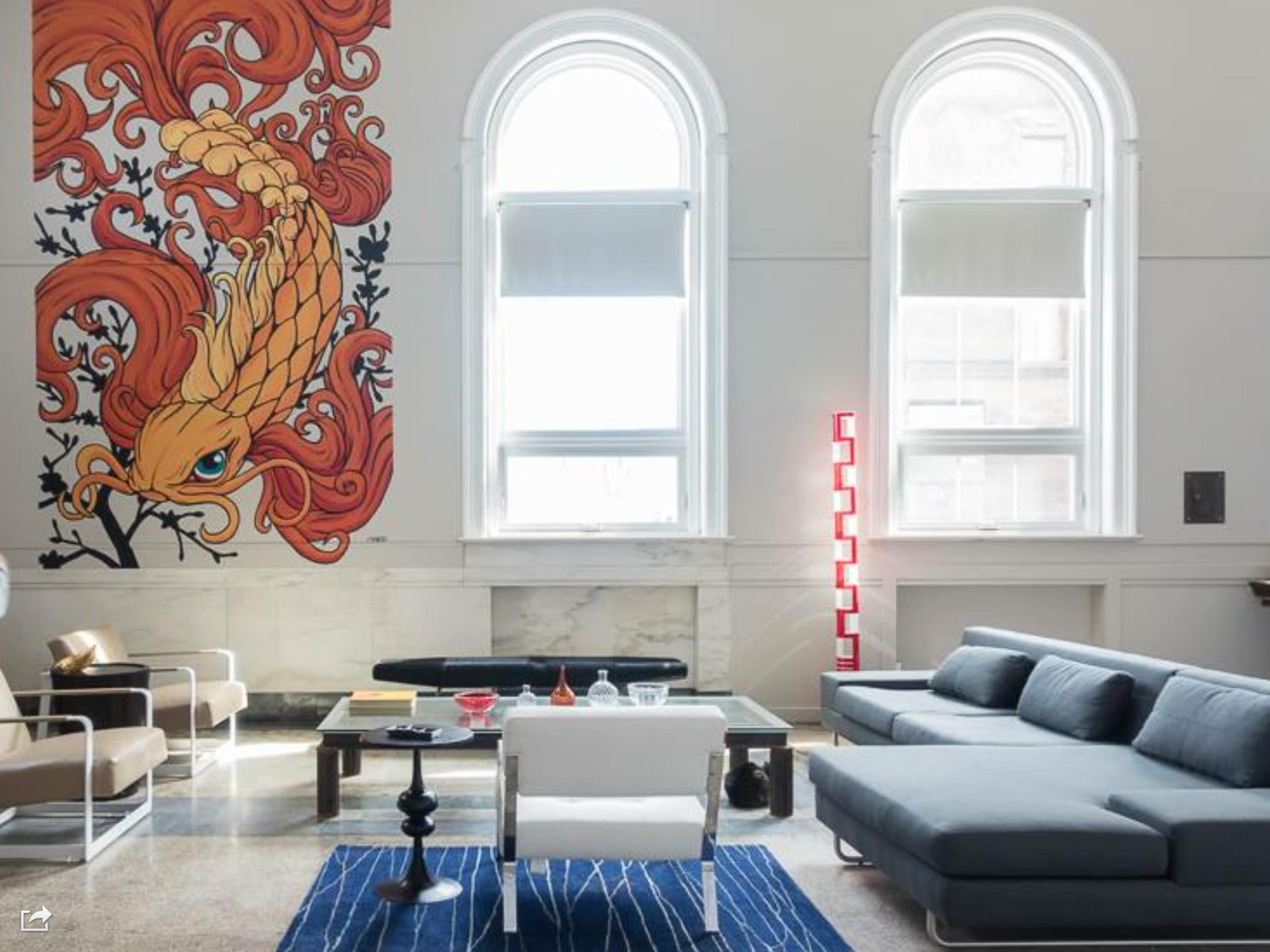 A modern living room featuring a large mural of a stylized orange phoenix on the wall, with a sectional sofa, a coffee table, and a combination of different seating arrangements.