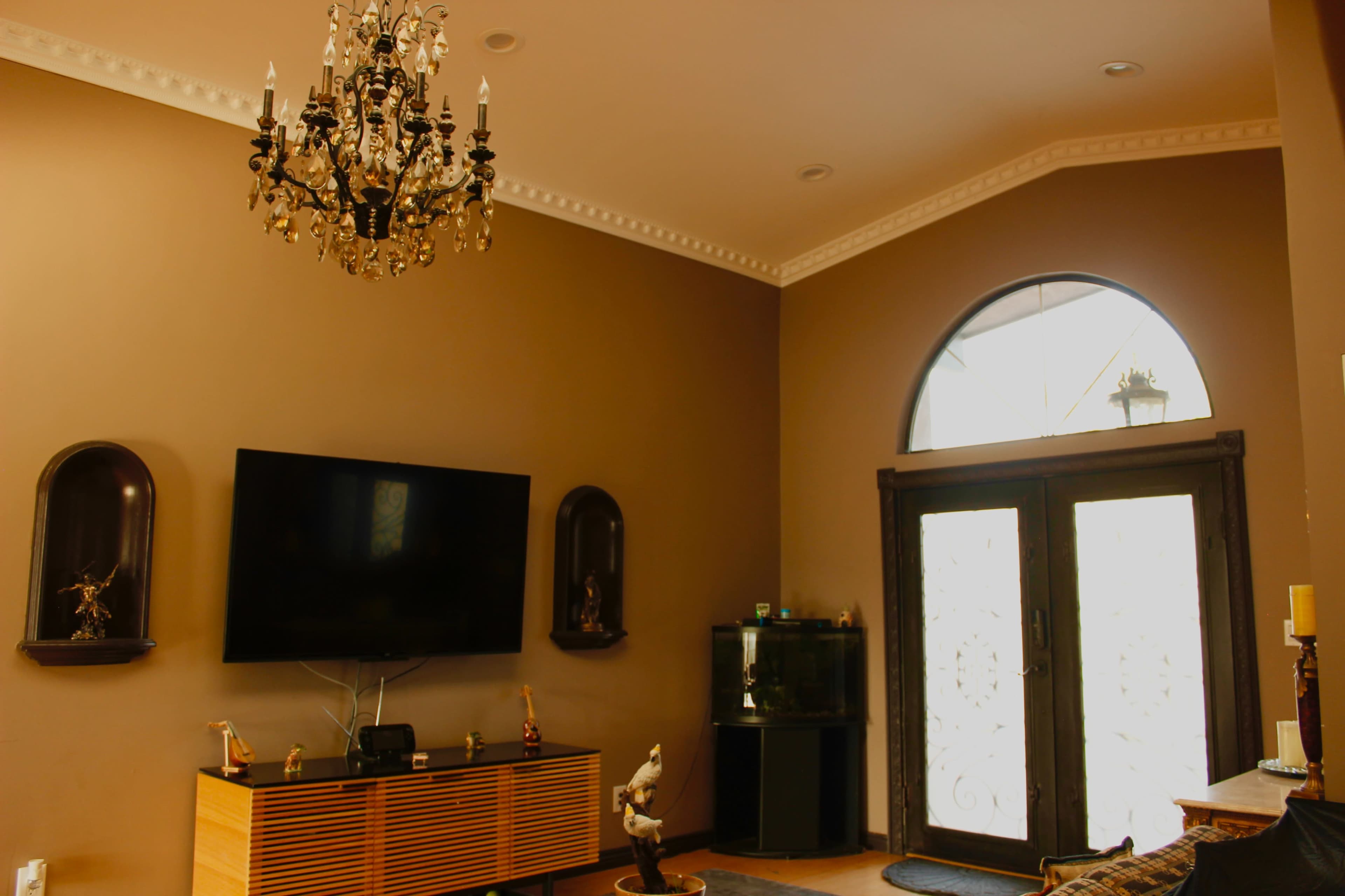A spacious living room features a chandelier, a large television mounted on the wall, and a set of double doors leading outside.