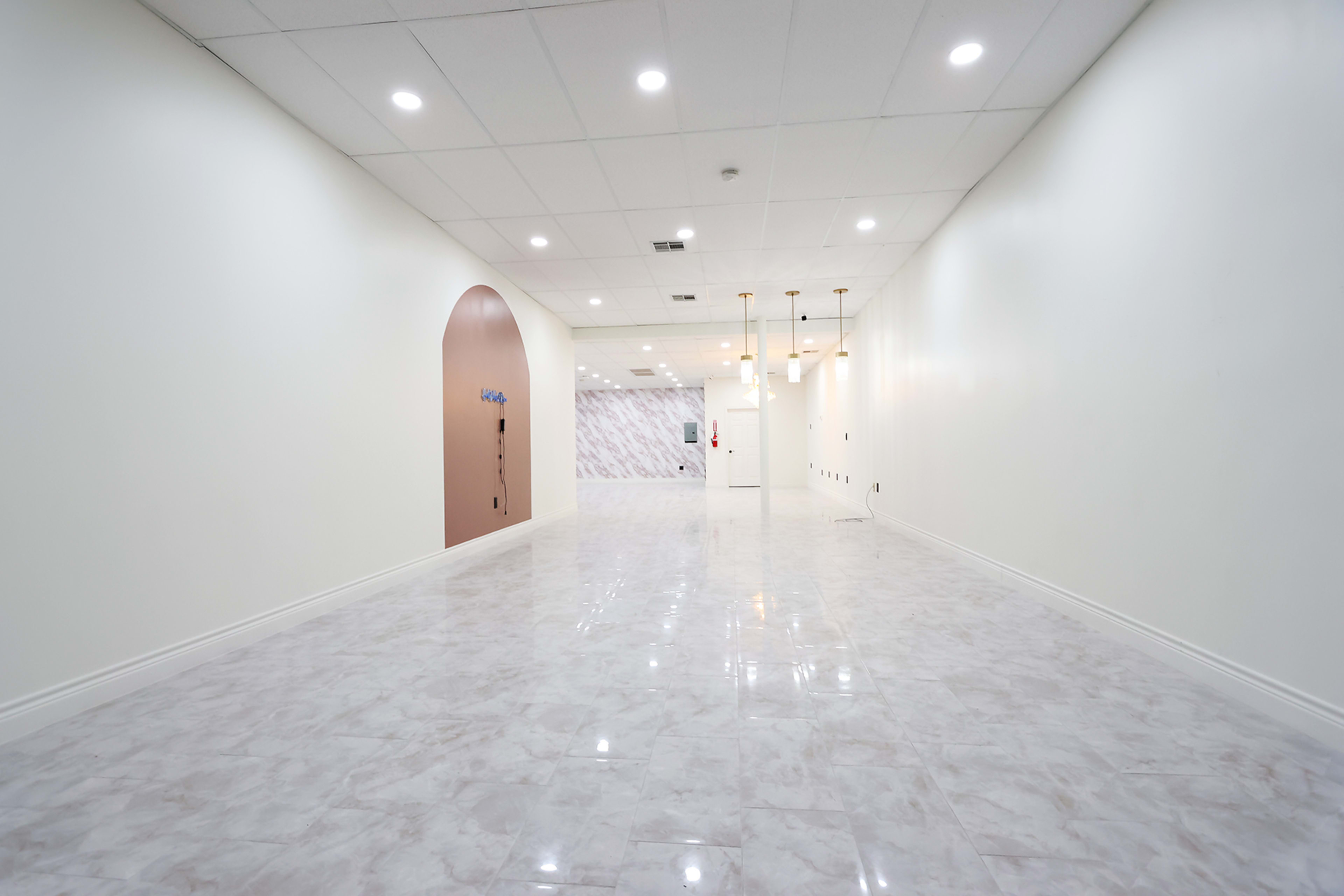 A spacious, well-lit hallway with white walls and shiny marble flooring, featuring decorative elements at one end.