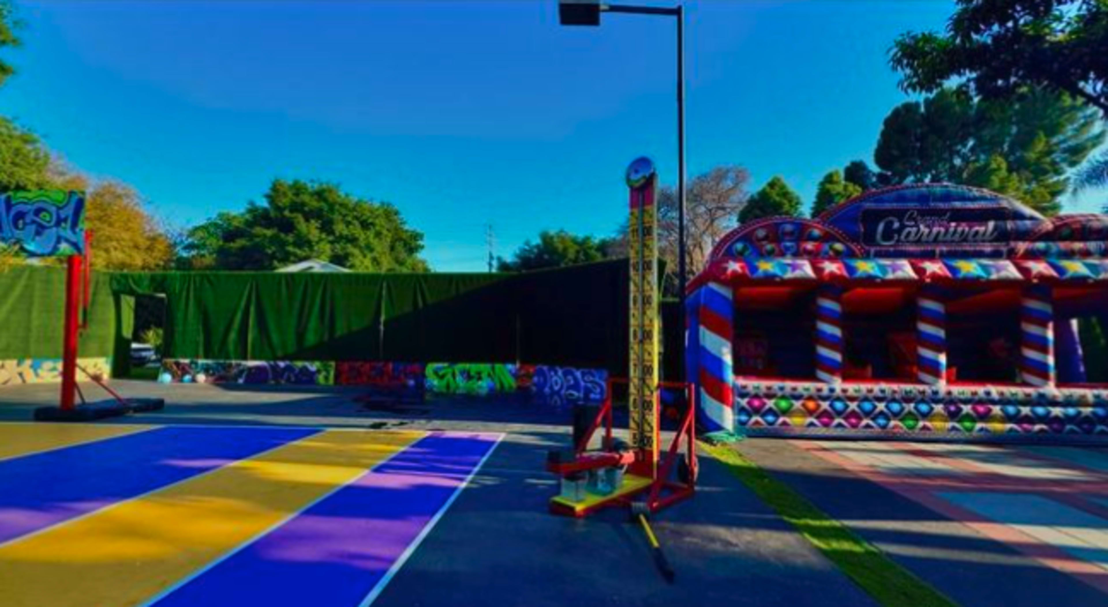 A vibrant outdoor activity area featuring a colorful court, a carnival-style booth, and a basketball hoop.