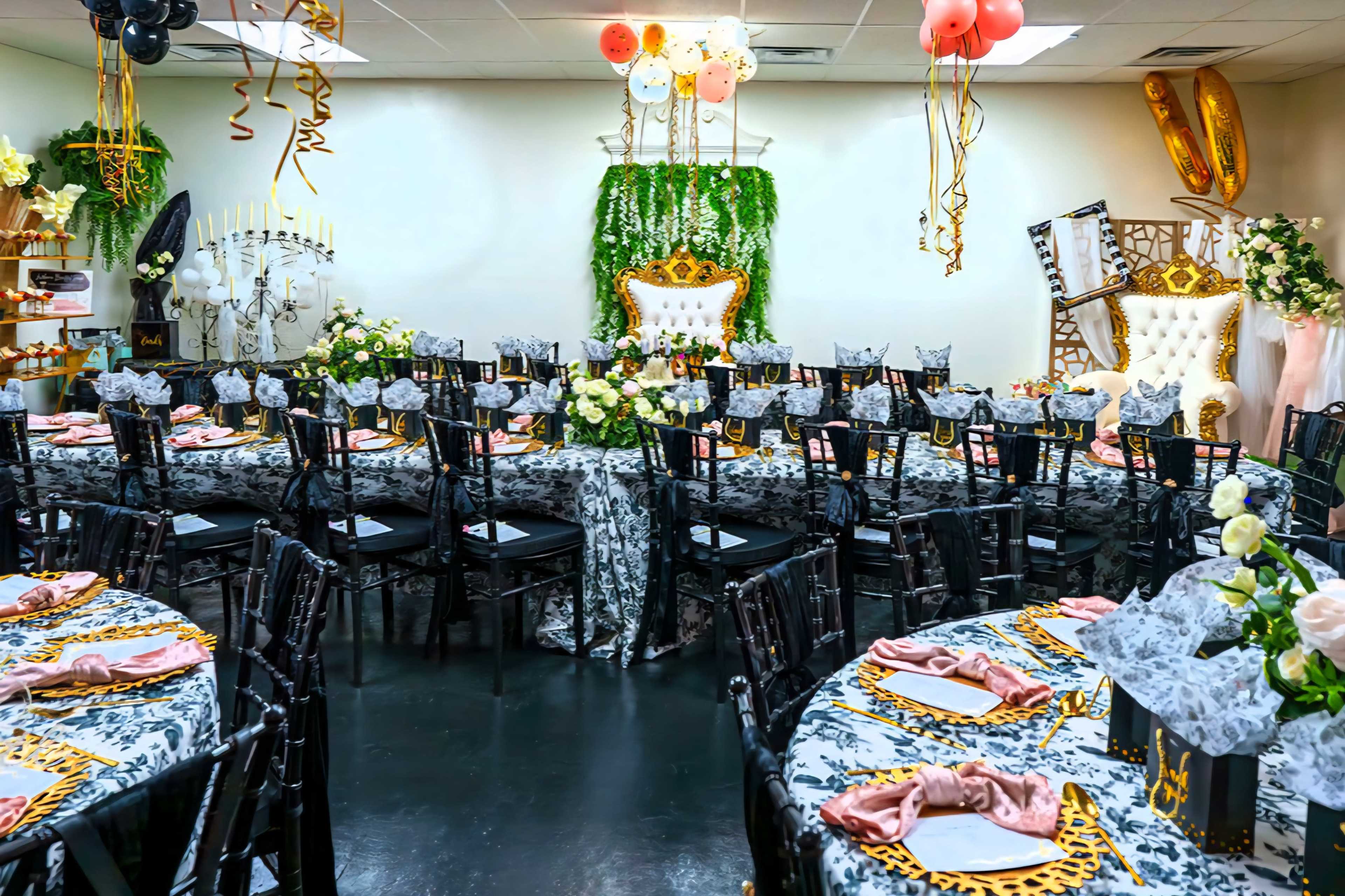 The image shows a decorated banquet hall with multiple tables set for a formal event, complete with black chairs, floral centerpieces, and a gold and white throne at the front.