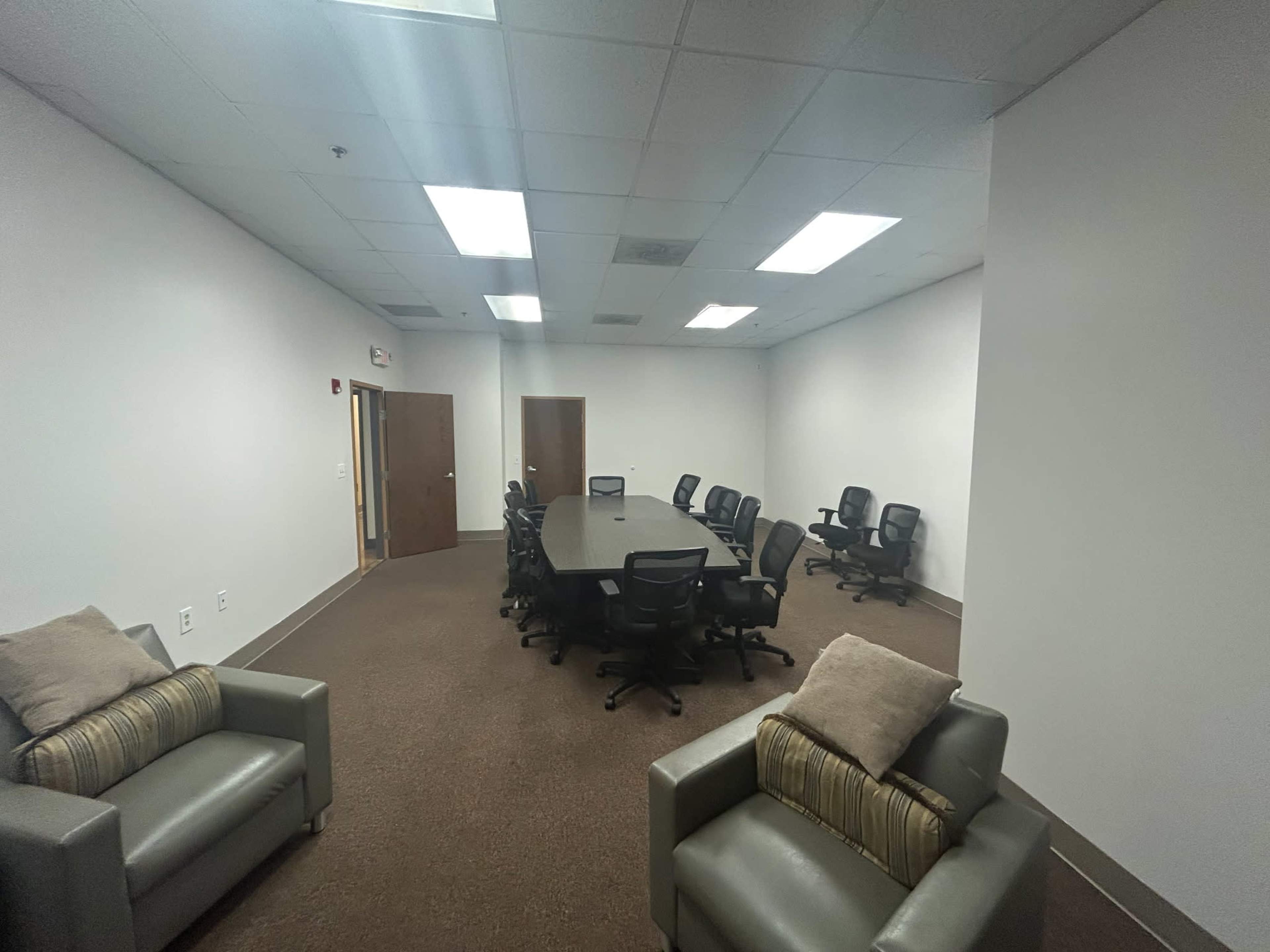 The image shows a conference room with a long table surrounded by multiple office chairs and two armchairs positioned against the wall.