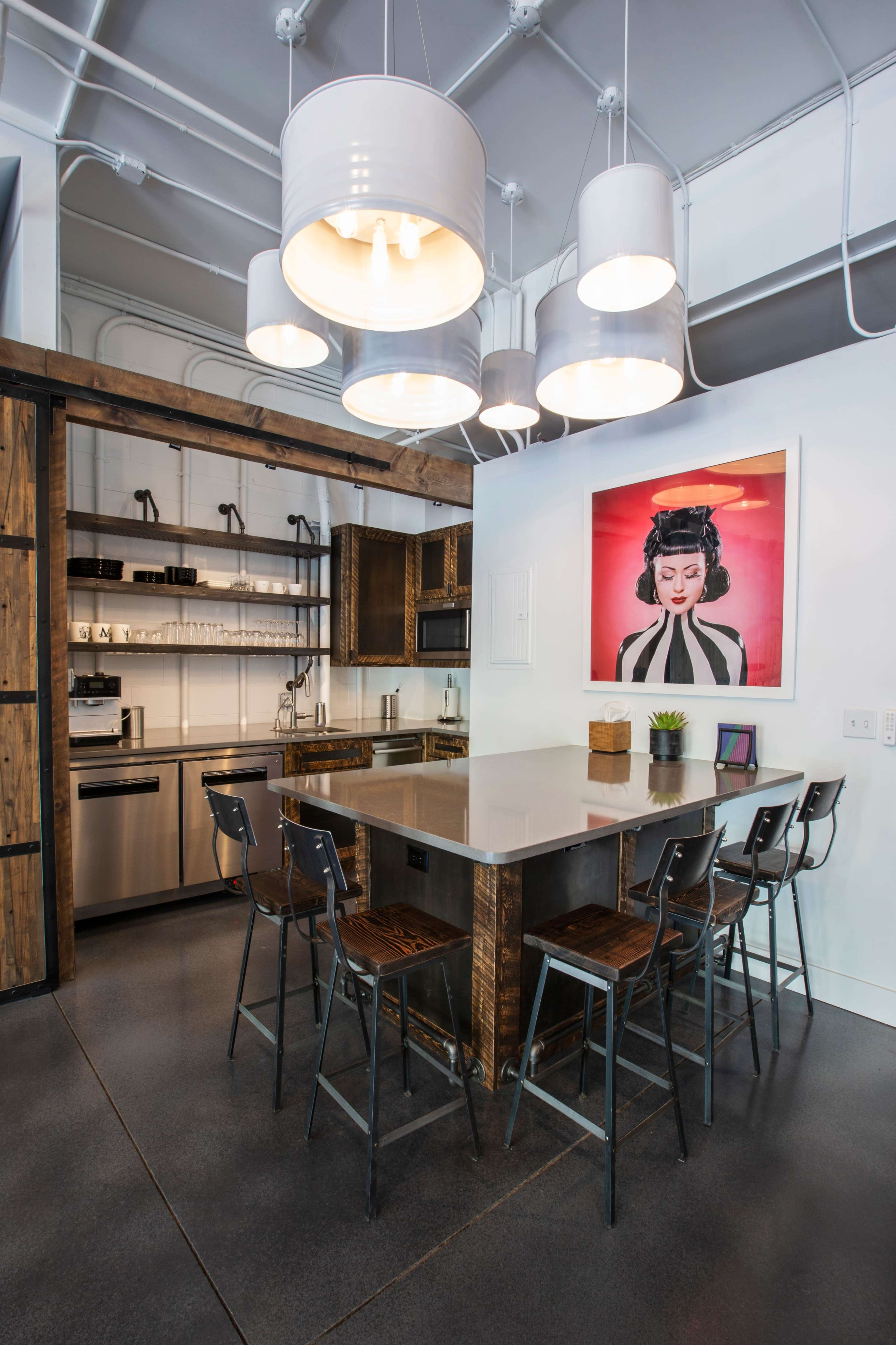 The image shows a modern kitchen with a large island, bar stools, stainless steel appliances, and a framed artwork on the wall.