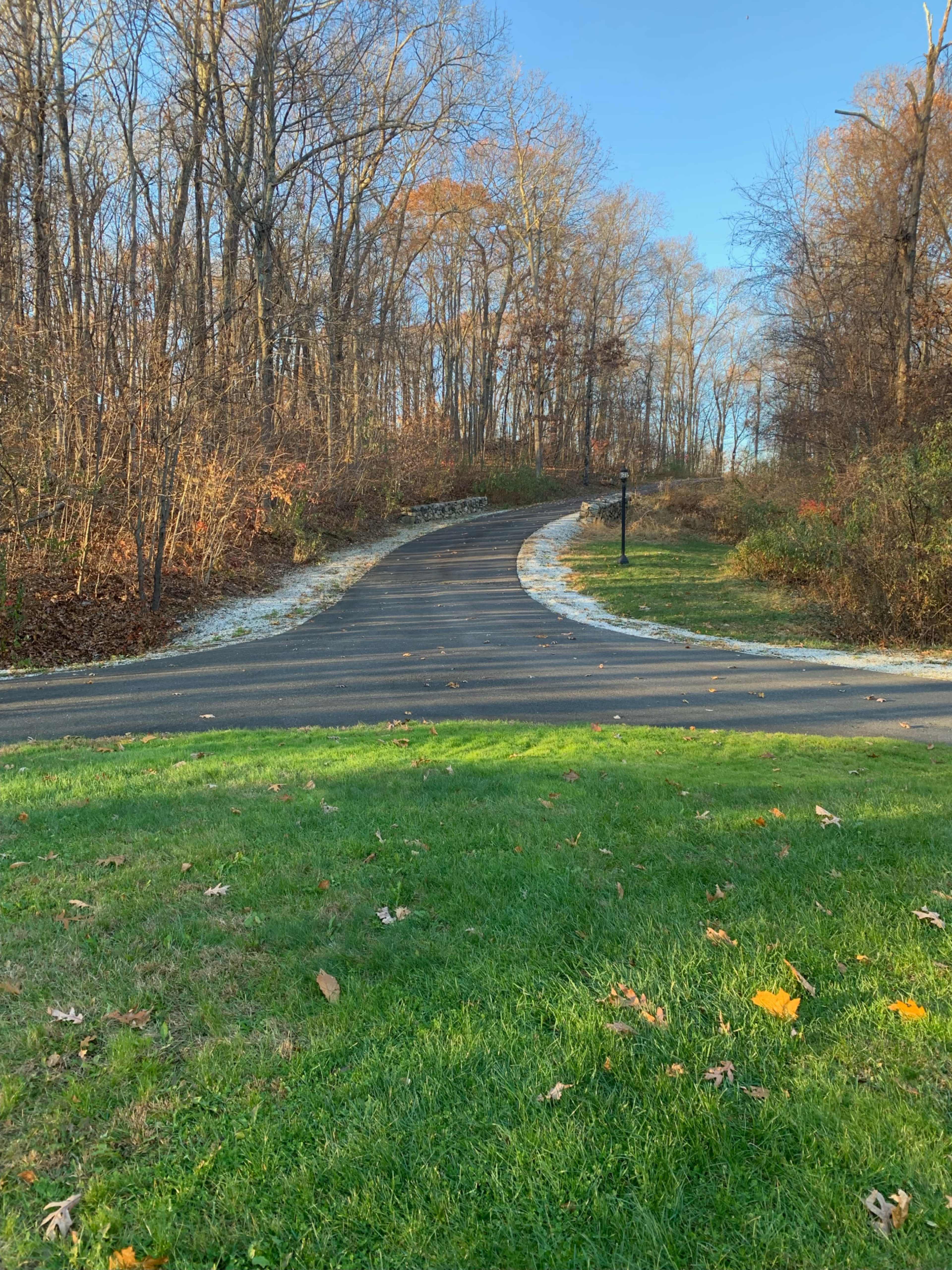 A winding asphalt path leads through a wooded area with autumn foliage on either side.