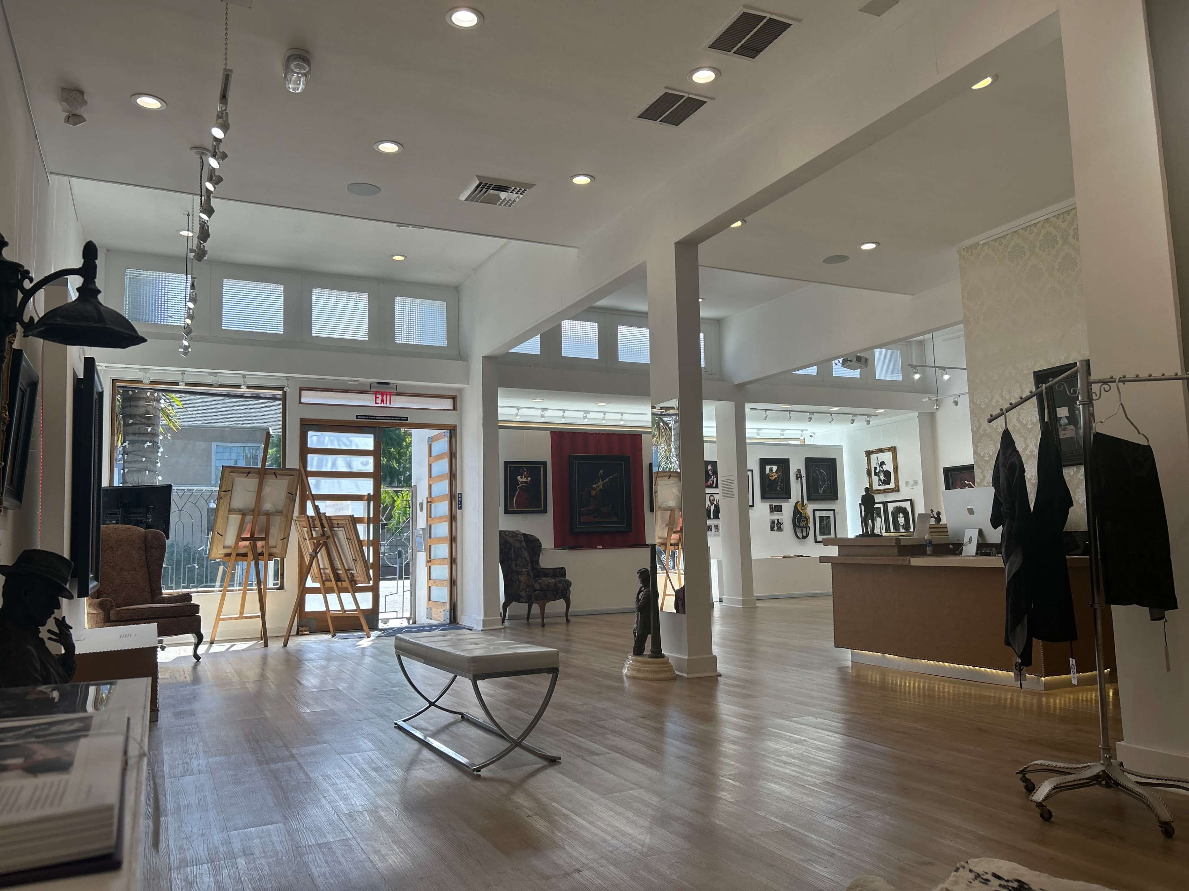 The image shows the interior of an art gallery featuring a spacious layout, art displays on the walls, and an open area with furniture and sculptures.