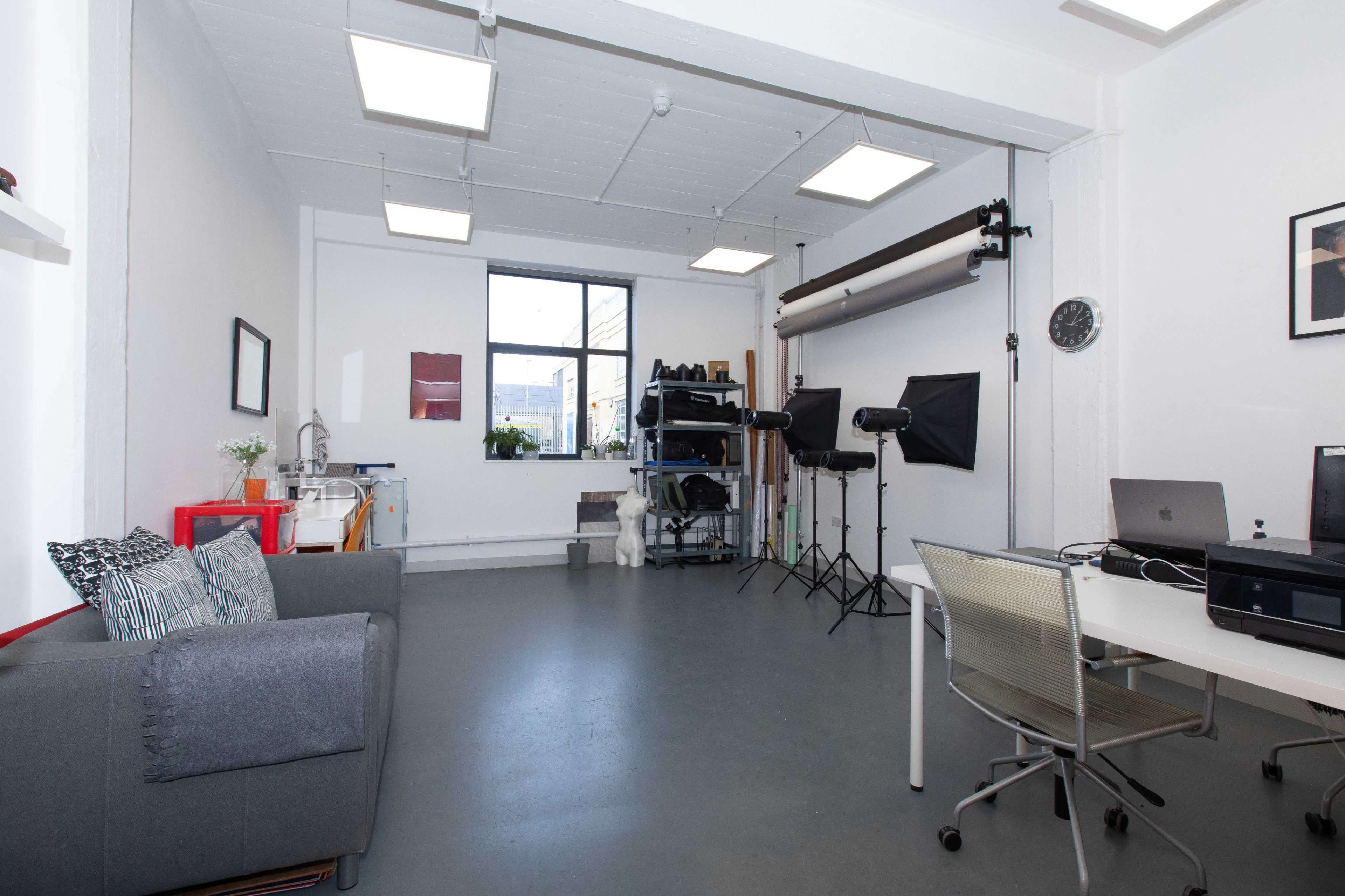 A spacious studio with a gray sofa, a desk with computers, and equipment for photography set up against the walls.