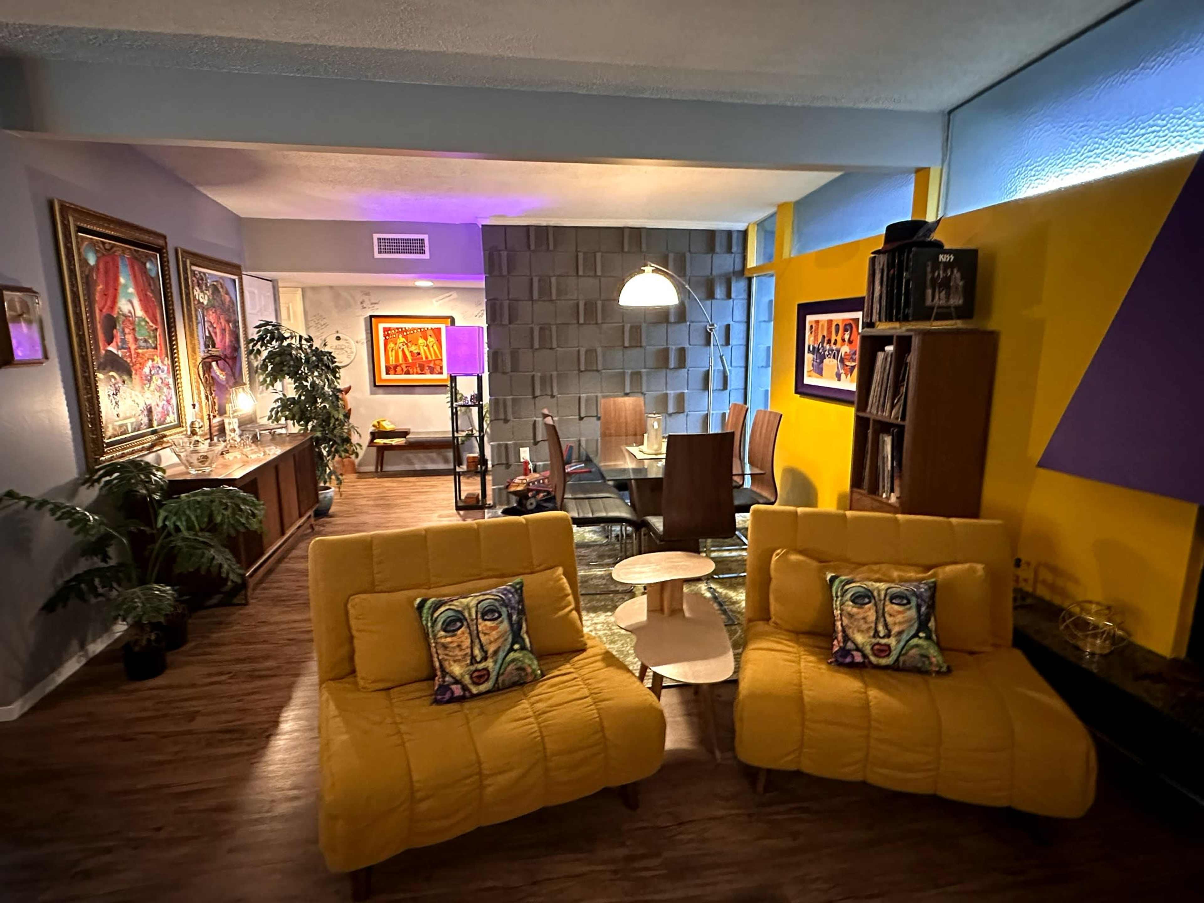 A modern living space with yellow lounge chairs, a dining area, and artwork on the walls.