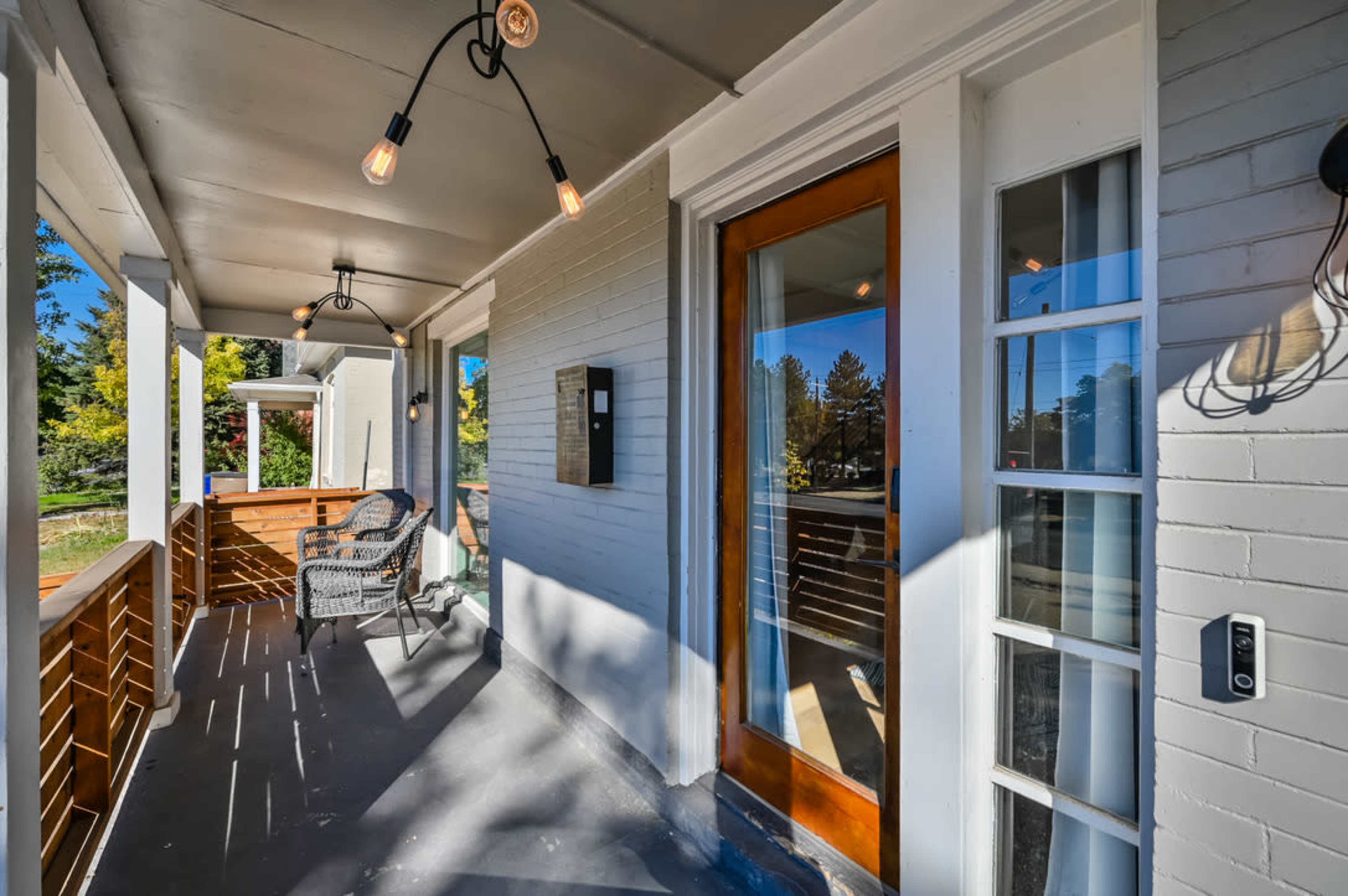 A covered porch with a wooden floor, a front door, and two light fixtures hanging from the ceiling.