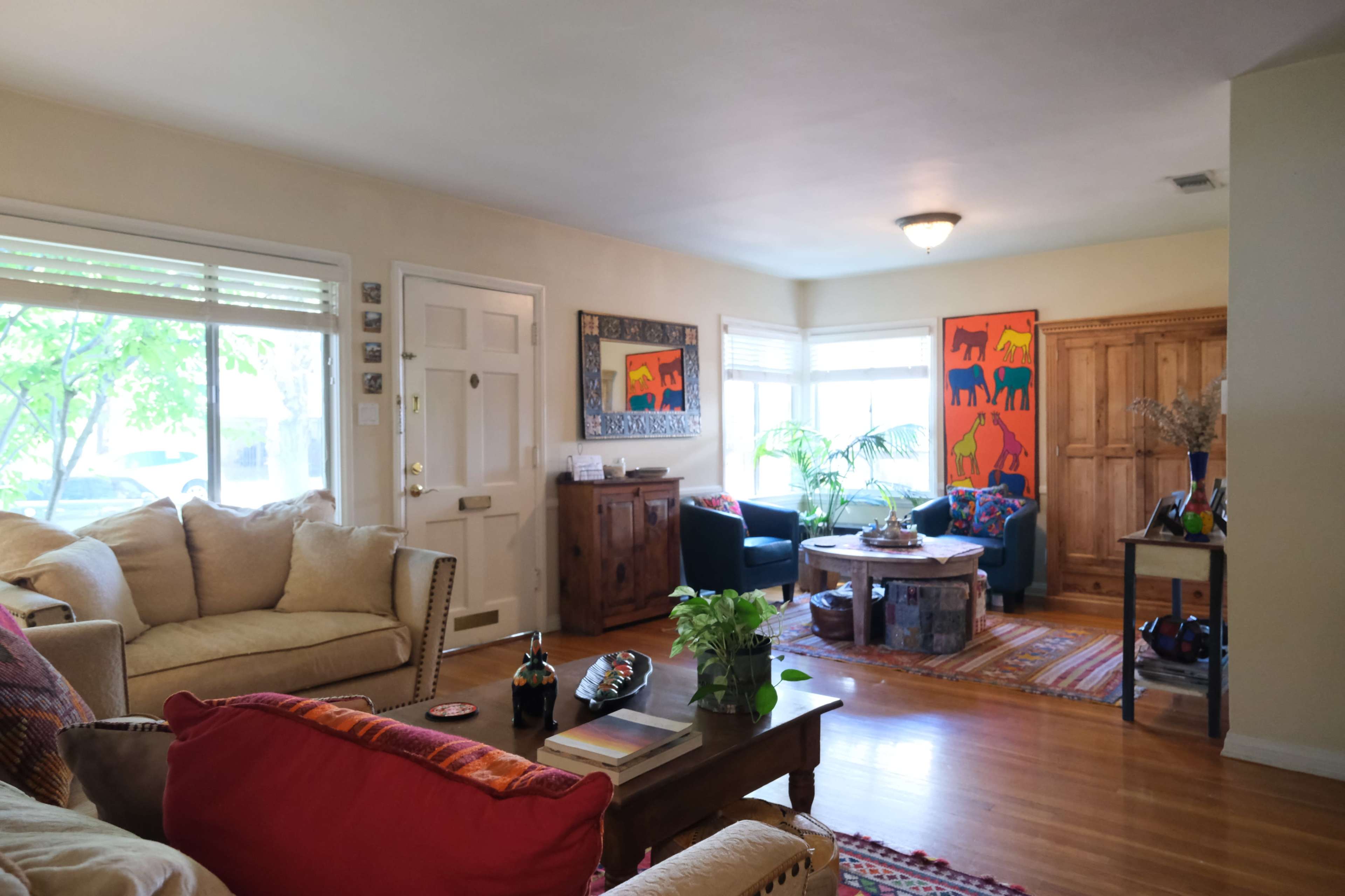 A cozy living room with a beige sofa, colorful artwork on the walls, and a wooden coffee table surrounded by armchairs.