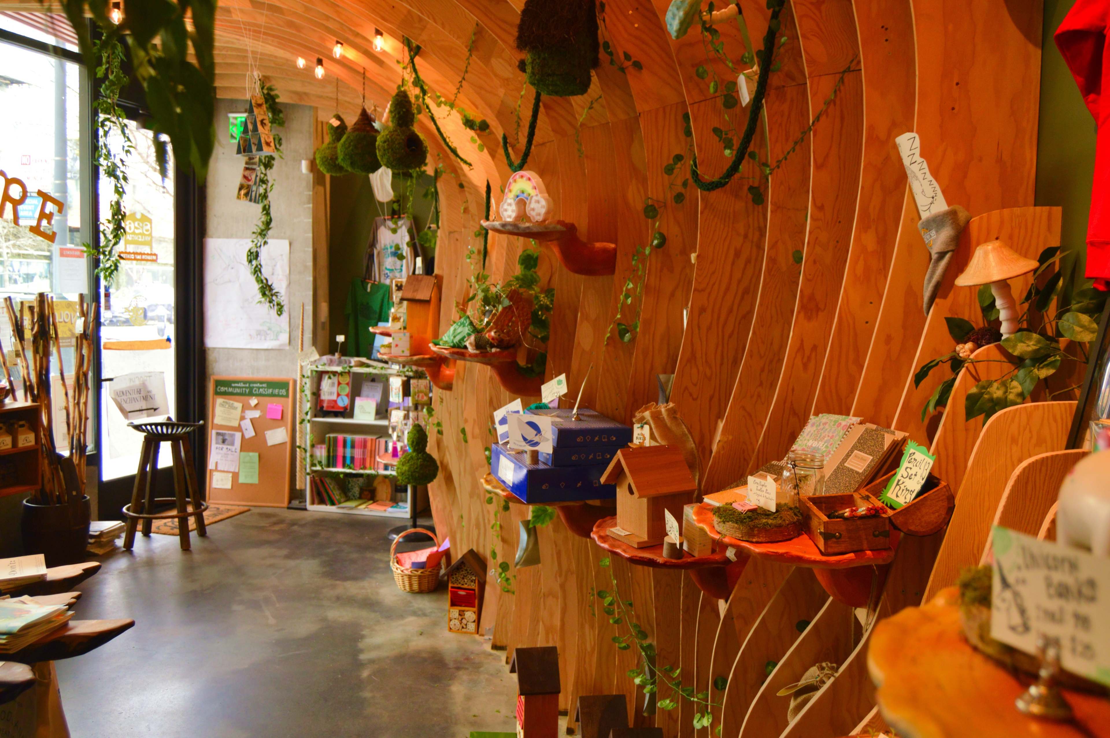 A wooden interior of a shop featuring shelves adorned with small houses, plants, and decorative items, along with a large window letting in natural light.