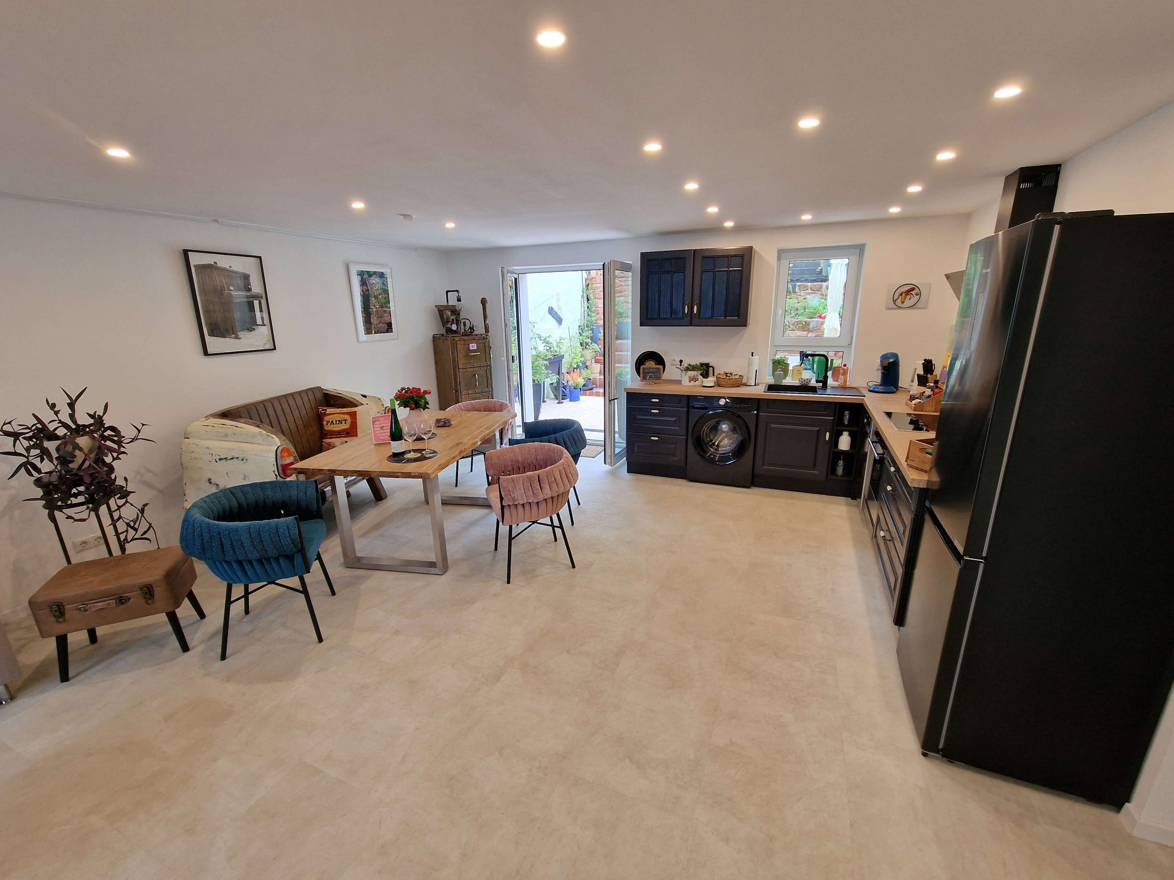 The image shows a modern kitchen with a dining area featuring a wooden table, colorful chairs, and a door leading to an outdoor space.