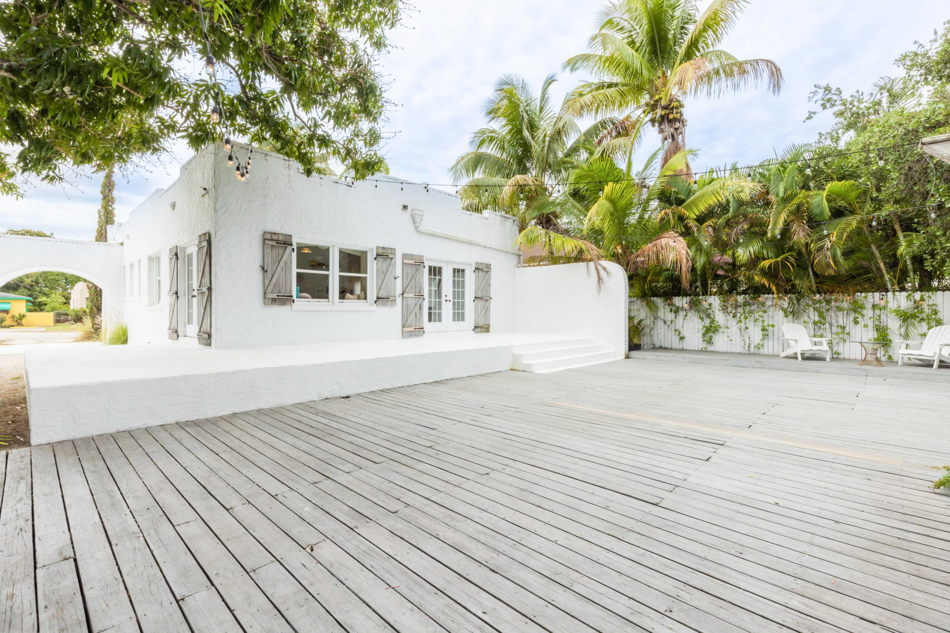 A white stucco house with wooden shutters surrounded by palm trees and a spacious wooden deck.