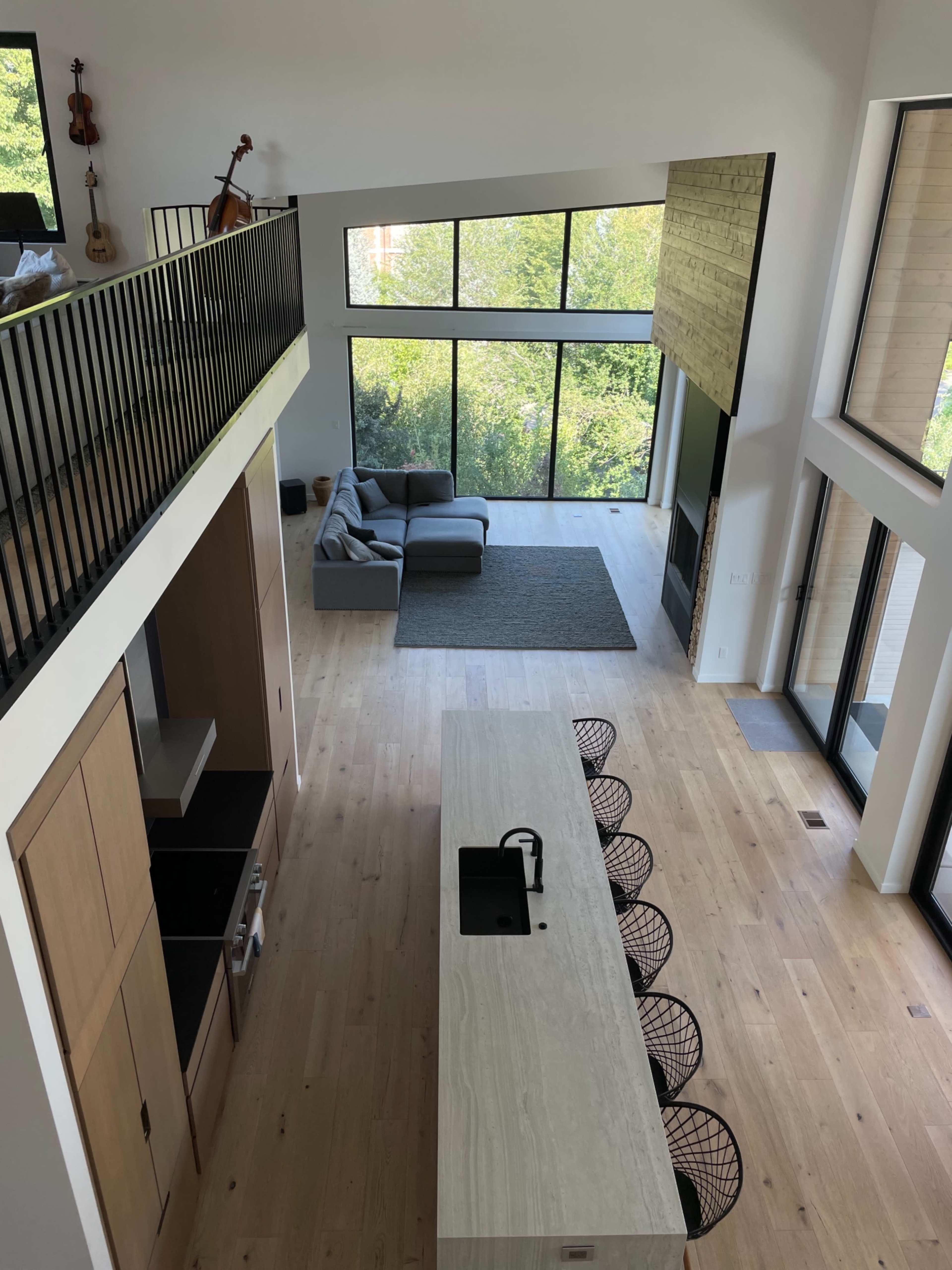 A spacious, modern home interior with a large kitchen island, a living area with a gray sofa, and large windows overlooking greenery.