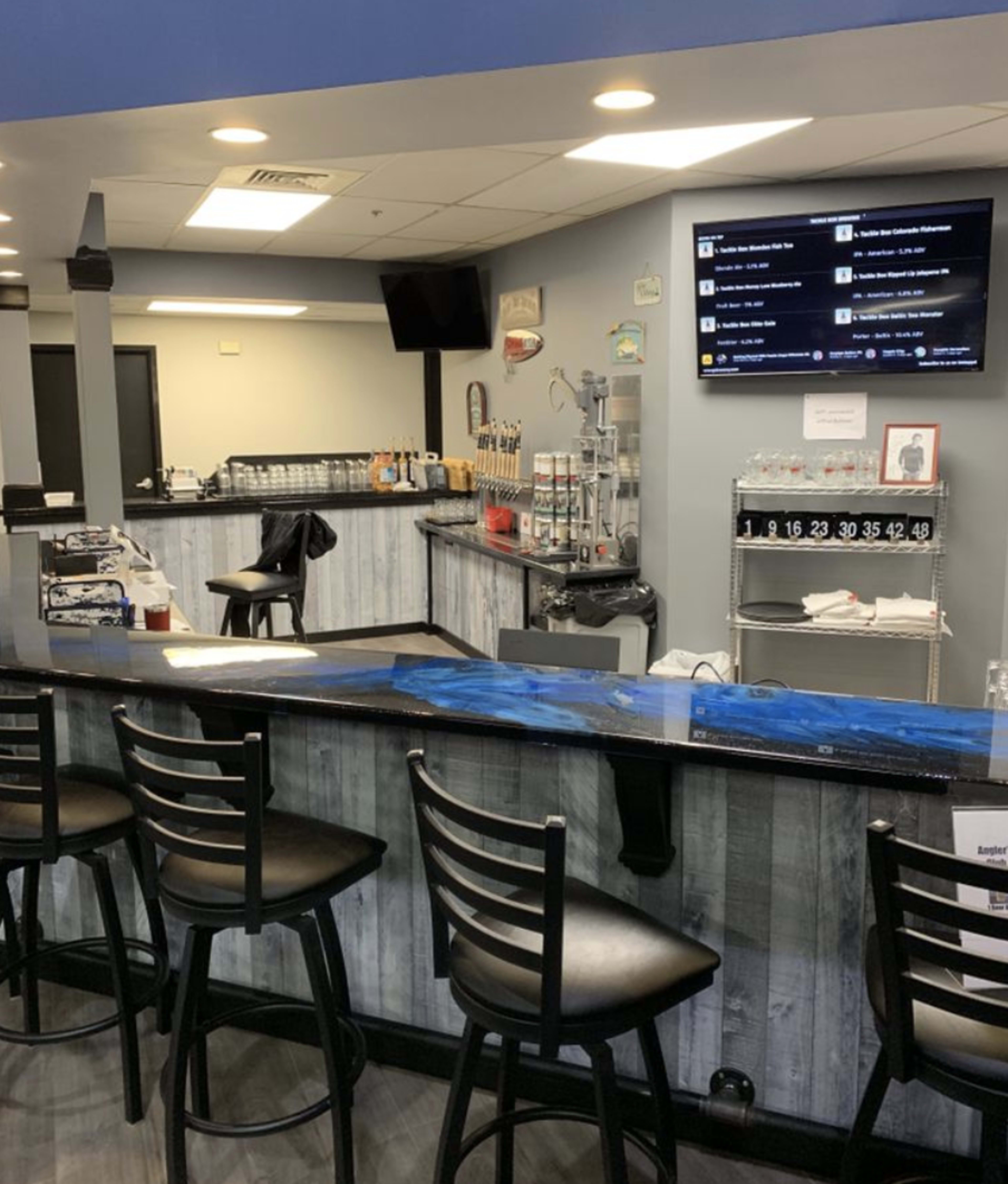 A modern bar area features a long counter with black stools, a variety of beer taps, and a television mounted on the wall.