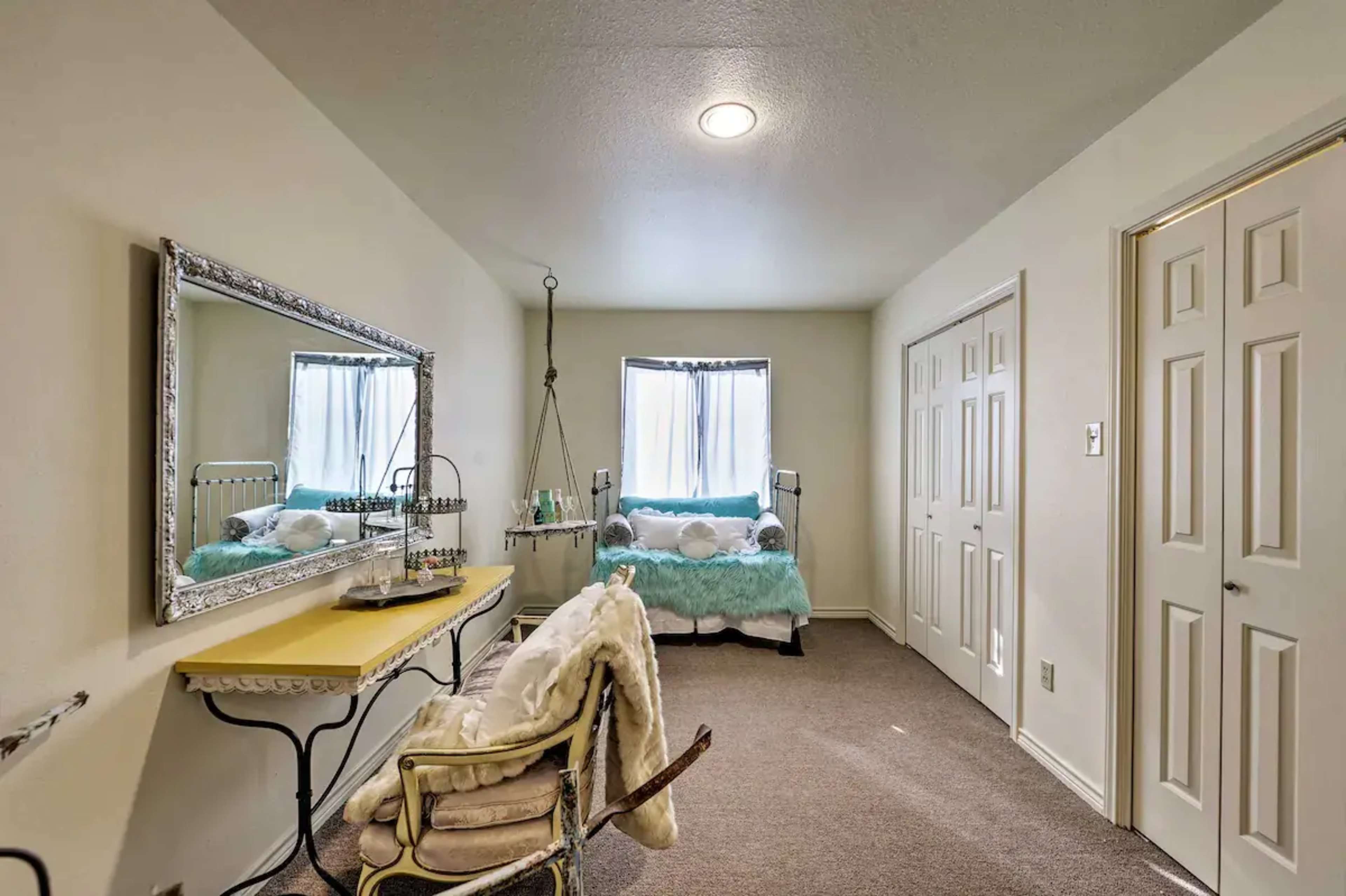 A spacious room features a bed with light blue bedding, a large mirror, and a small table with a chair.