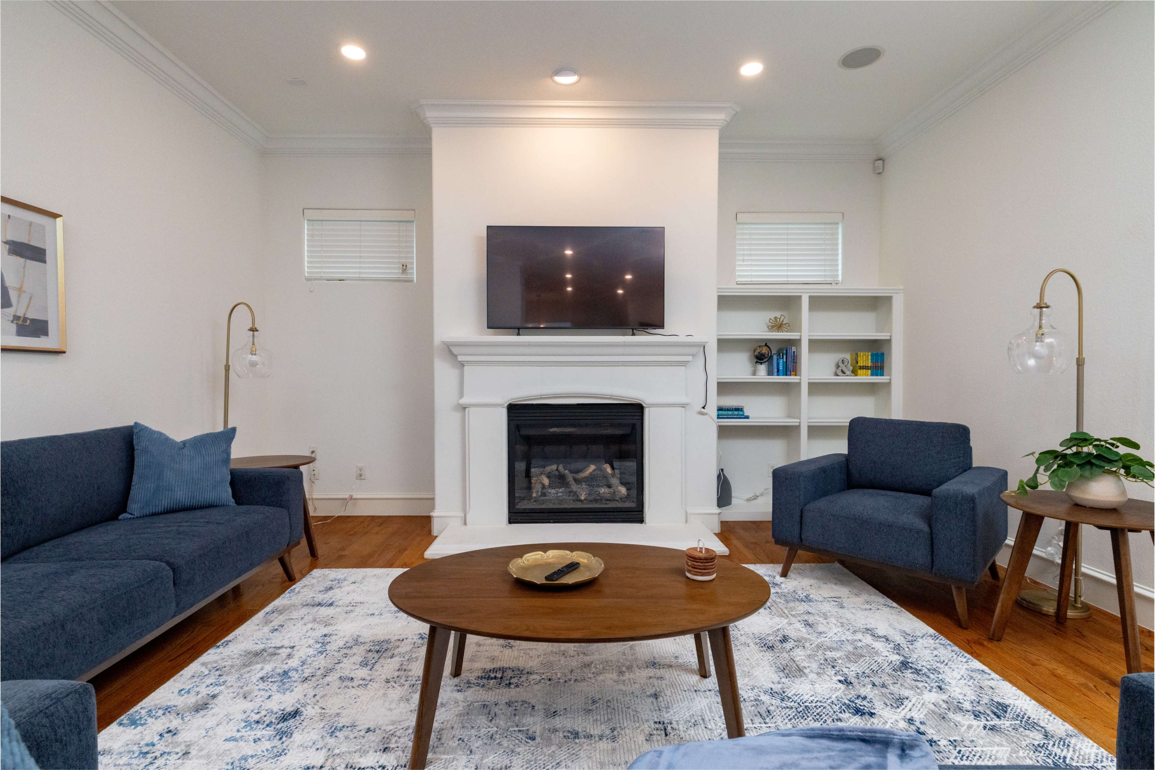 The living room features a fireplace with a television mounted above it, surrounded by blue furniture and a wooden coffee table on a patterned rug.