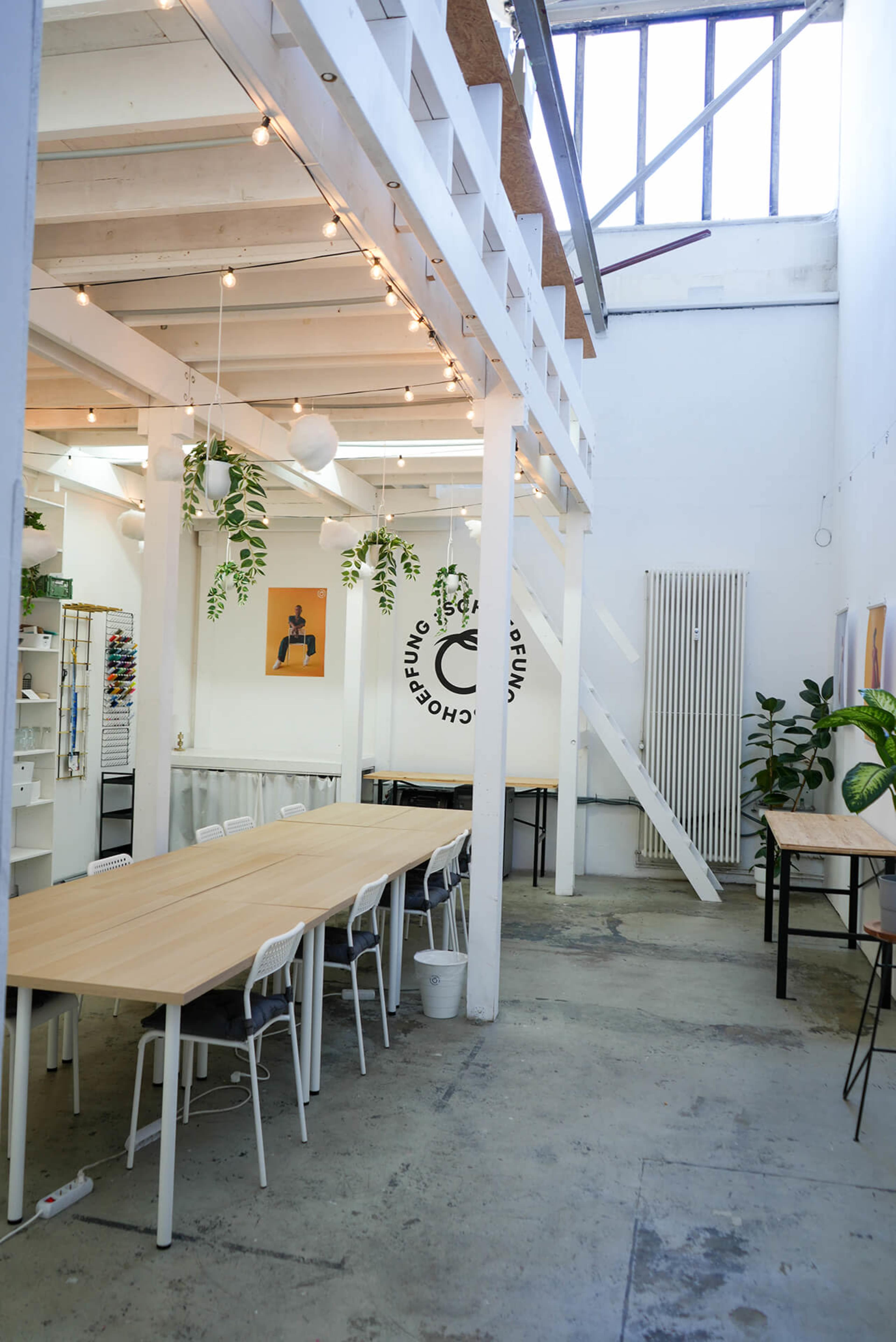 A spacious, well-lit interior with wooden tables, white walls, and plants hanging from the ceiling.