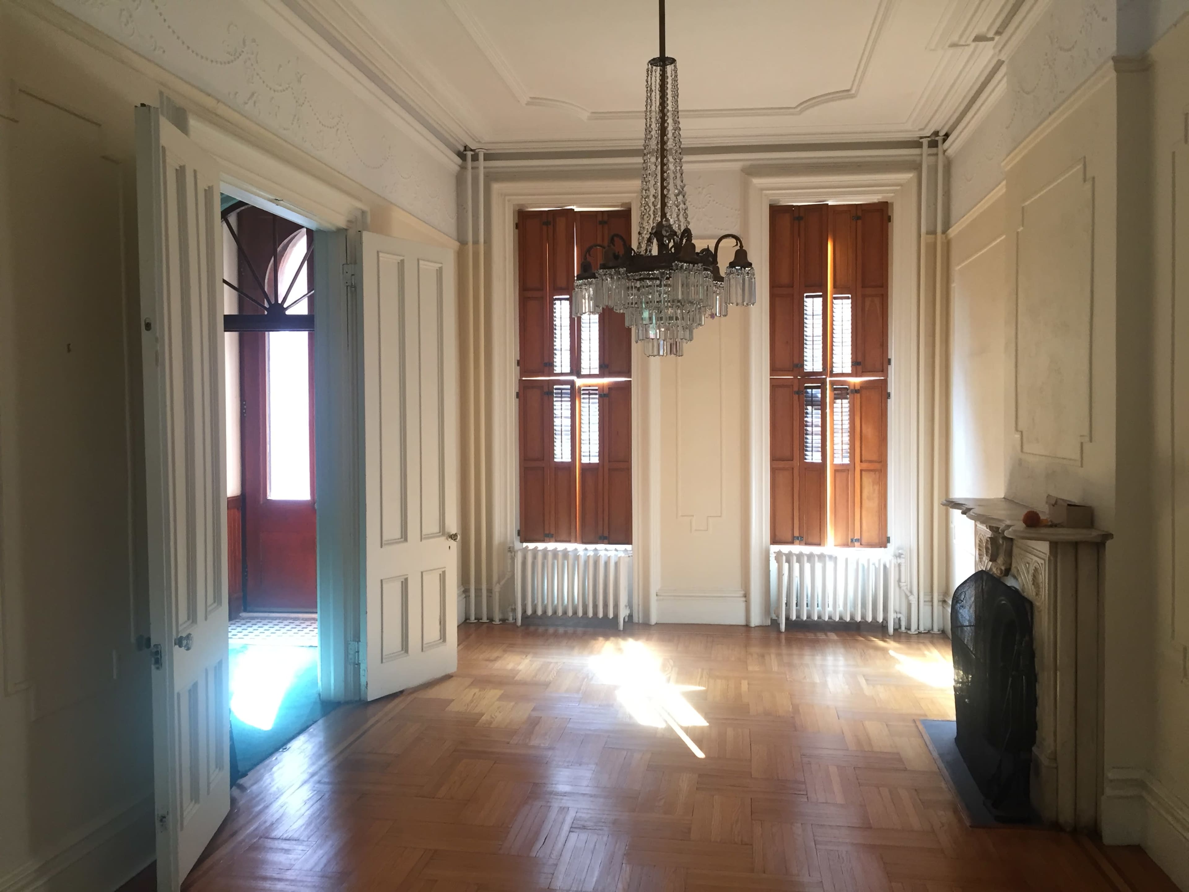 A spacious room with wooden floors, tall windows, and a chandelier, featuring doorways leading to another area.