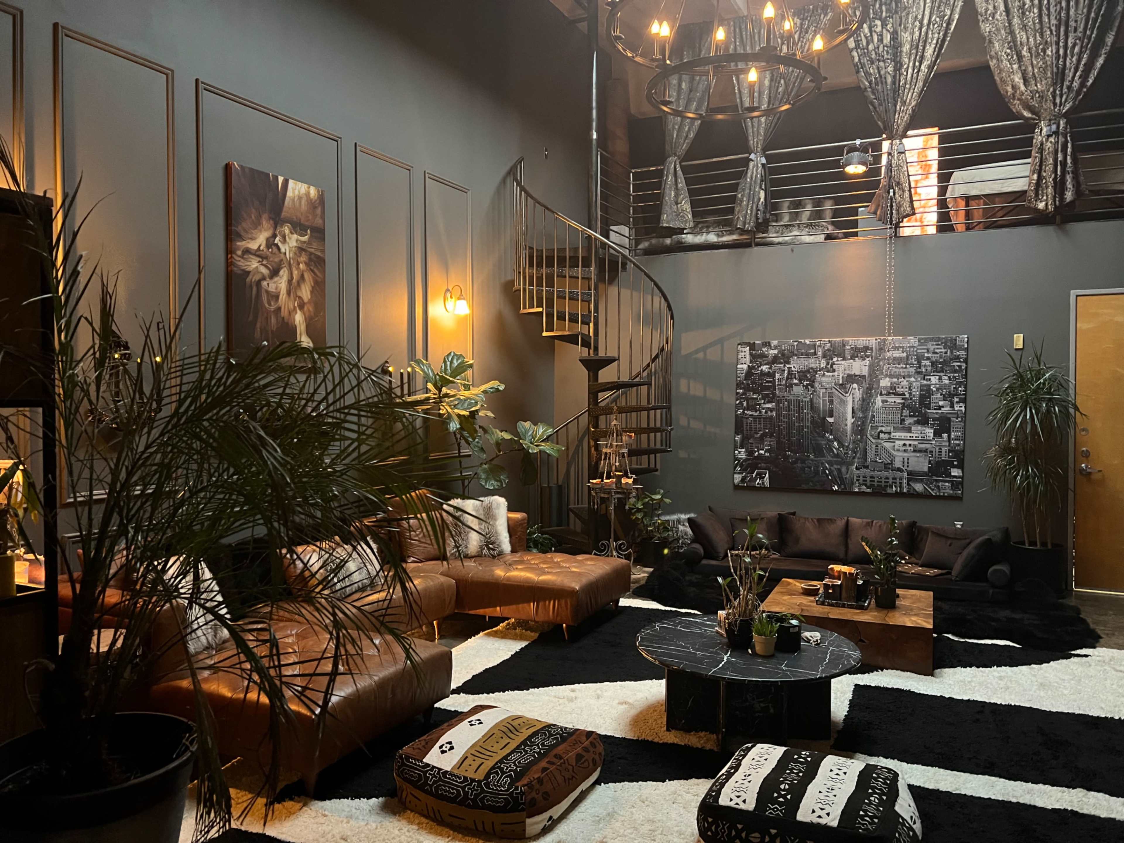 A stylish, modern living room with leather sofas, a circular staircase, and large plants, featuring dark walls and contrasting furniture.