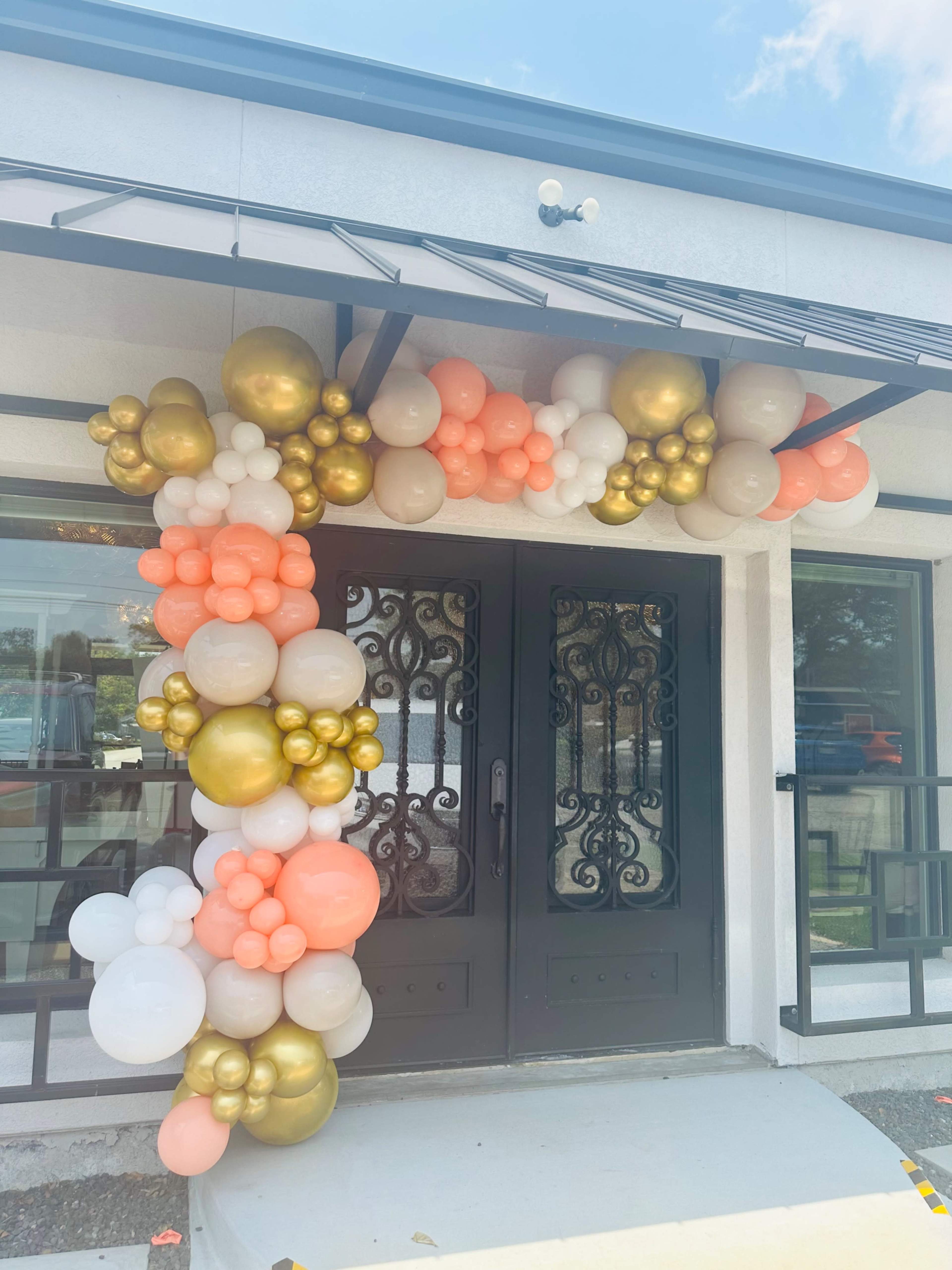 The entrance features a decorative arch made of various balloons in shades of peach, white, and gold.