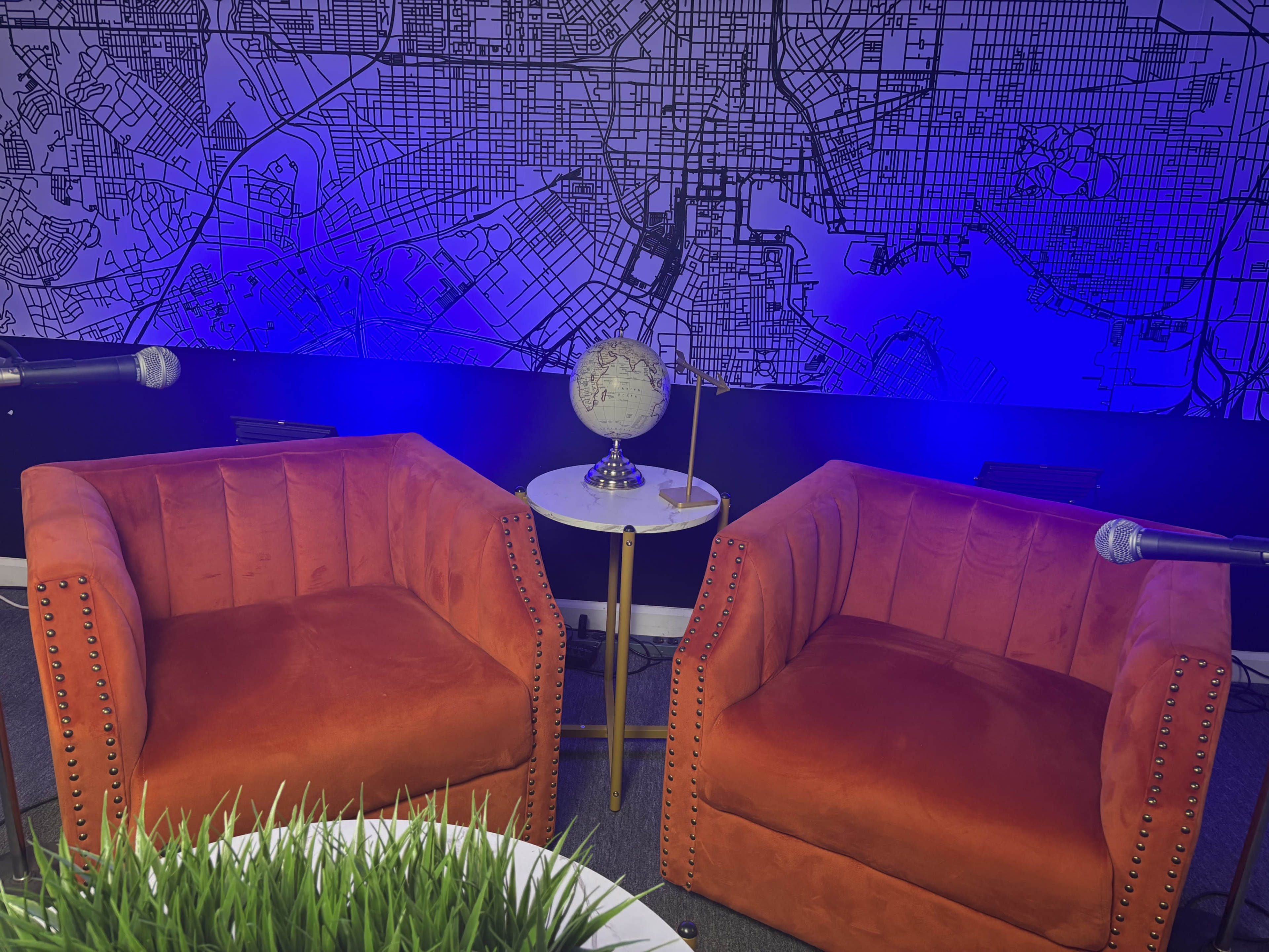 Two orange velvet chairs are positioned in front of a wall featuring a large map design, accompanied by a small round table with a globe and a lamp.