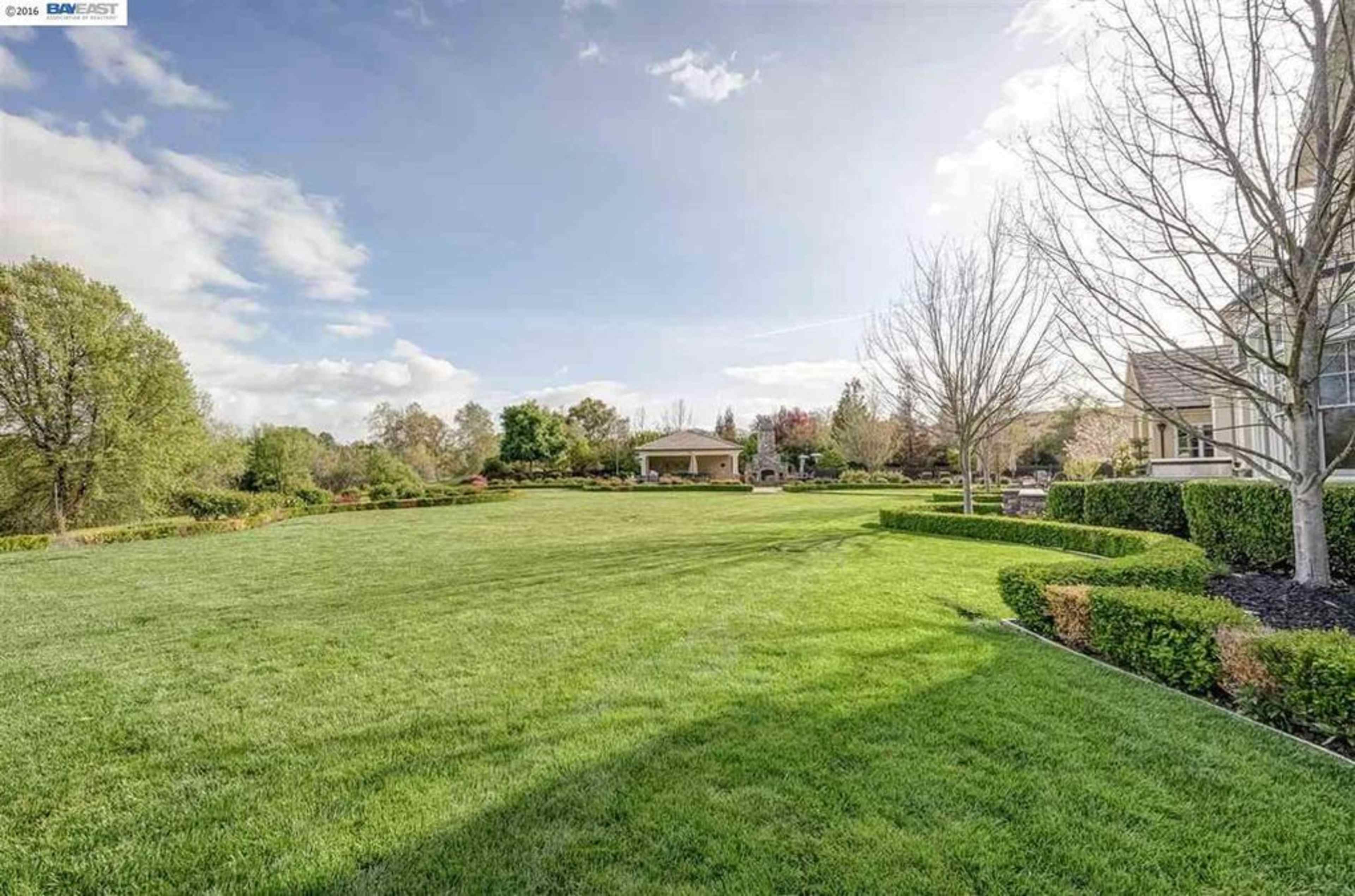 A spacious, well-maintained lawn surrounded by trees and a gazebo in a residential area.