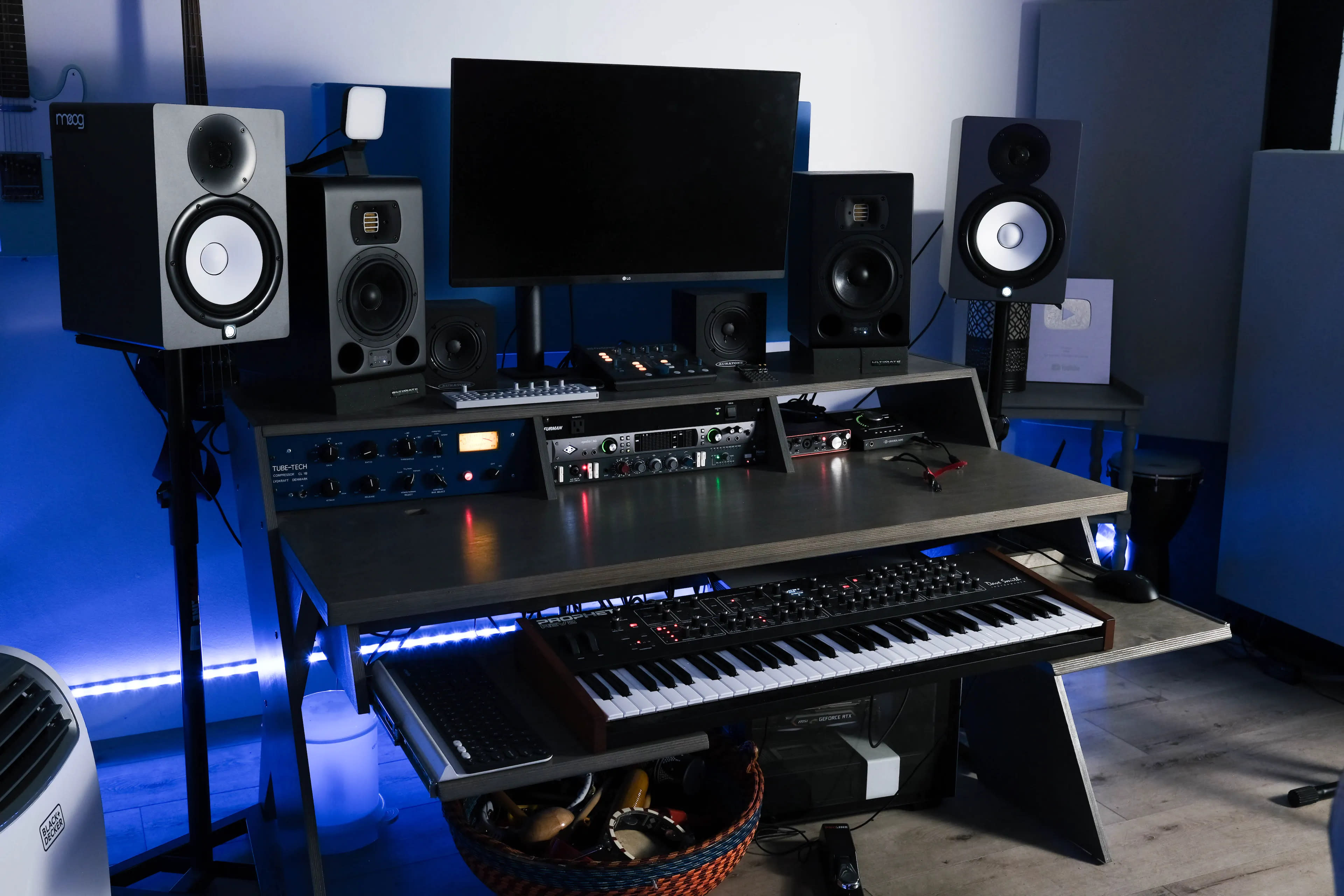 A music production setup featuring a desk with a keyboard, audio monitors, a computer screen, and various audio equipment.