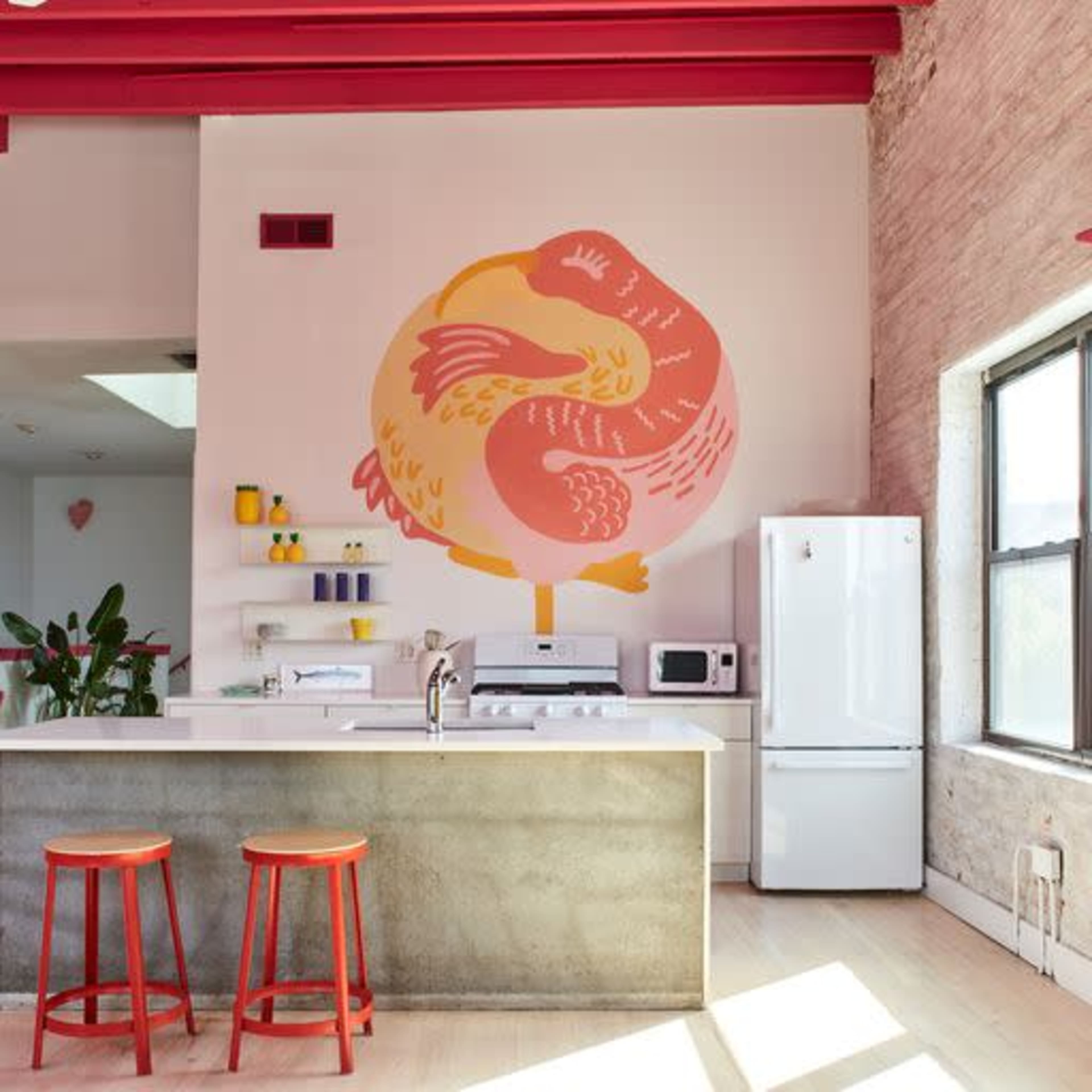 A modern kitchen features a large wall mural of a bird, with a concrete island and red bar stools.