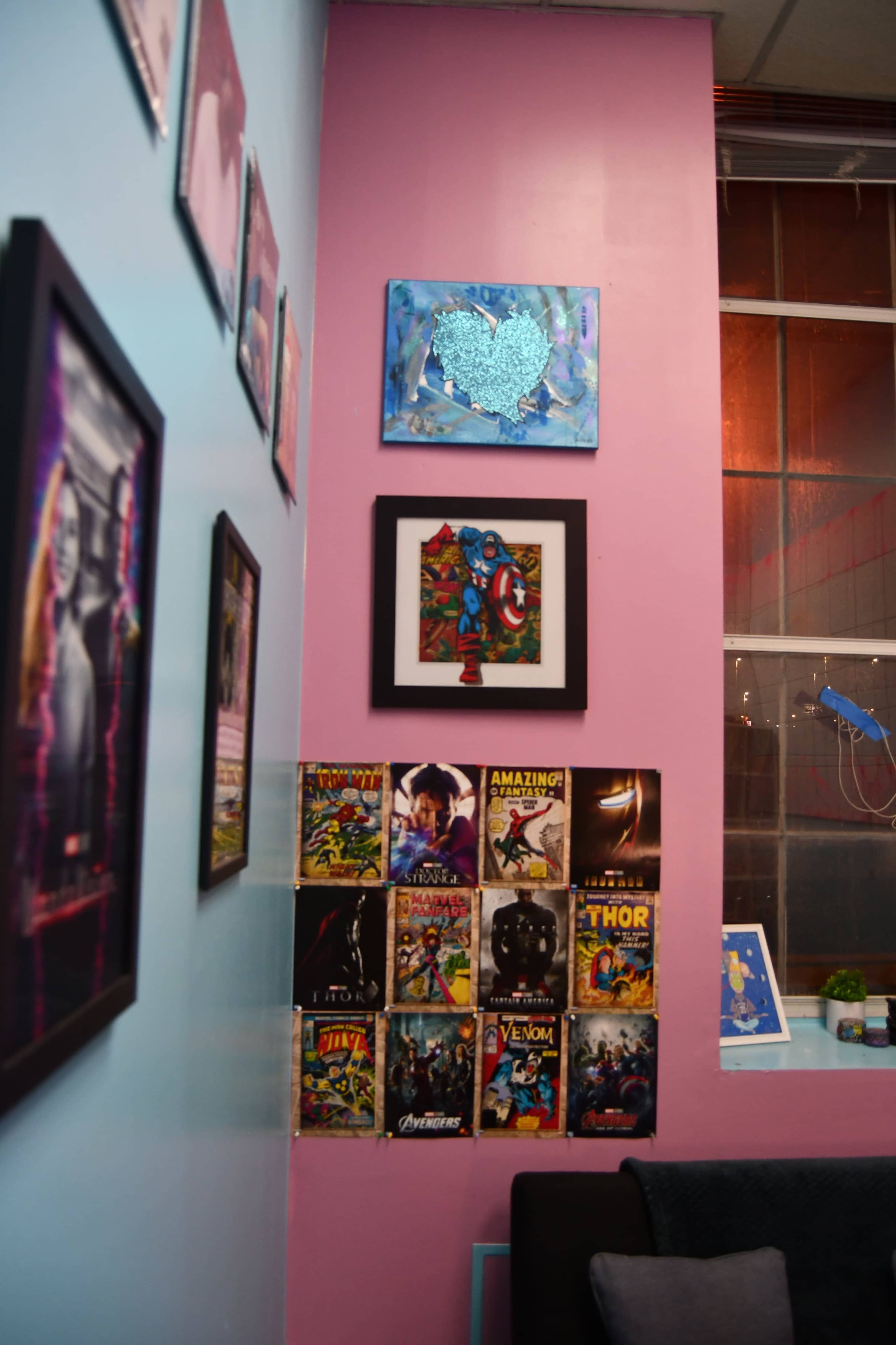 A colorful wall featuring framed artwork and comic book covers arranged in a visually appealing manner, with a large window in the background.
