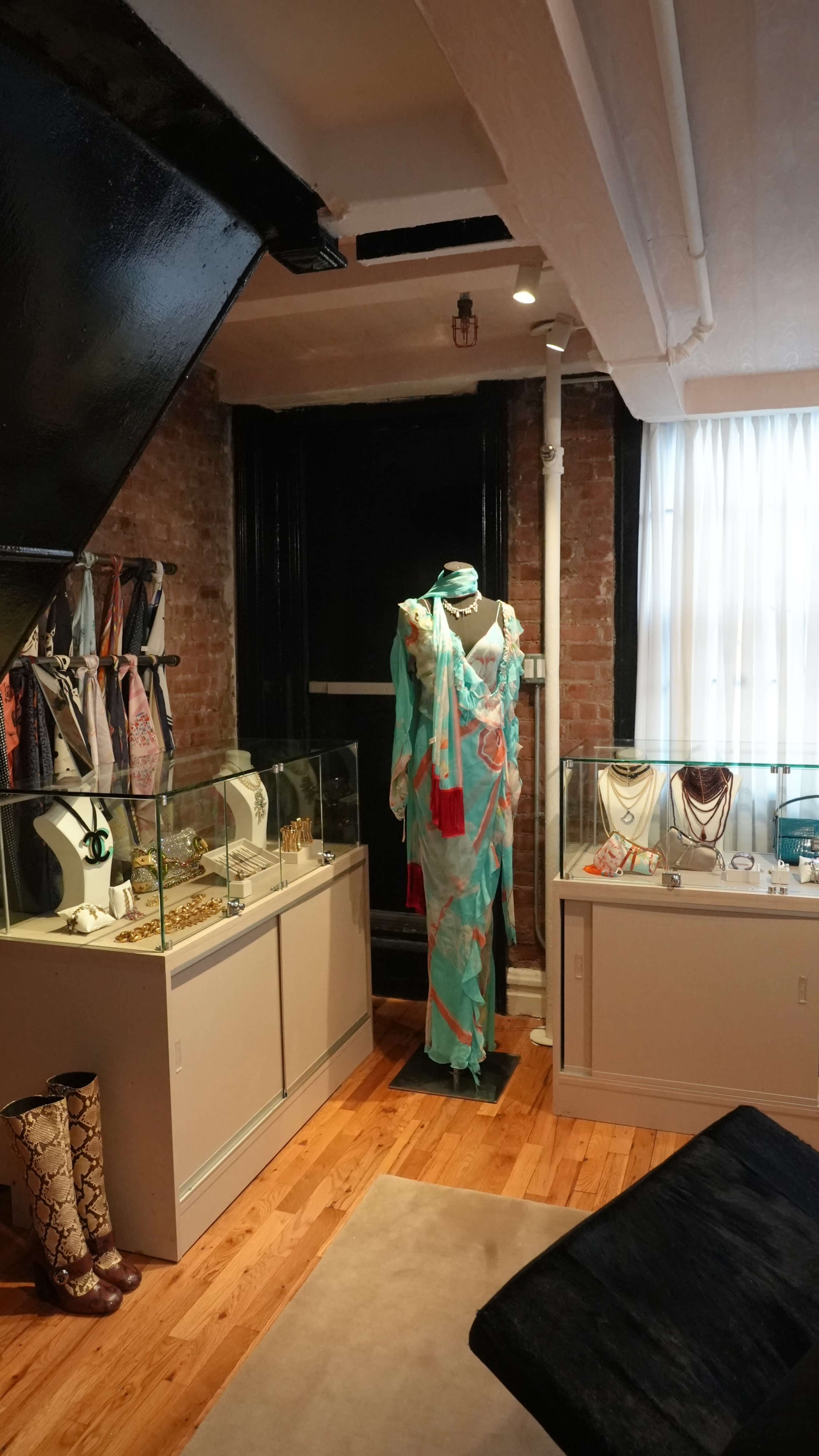 The image shows a boutique interior featuring a mannequin dressed in a colorful garment, surrounded by display cases showcasing jewelry and accessories.