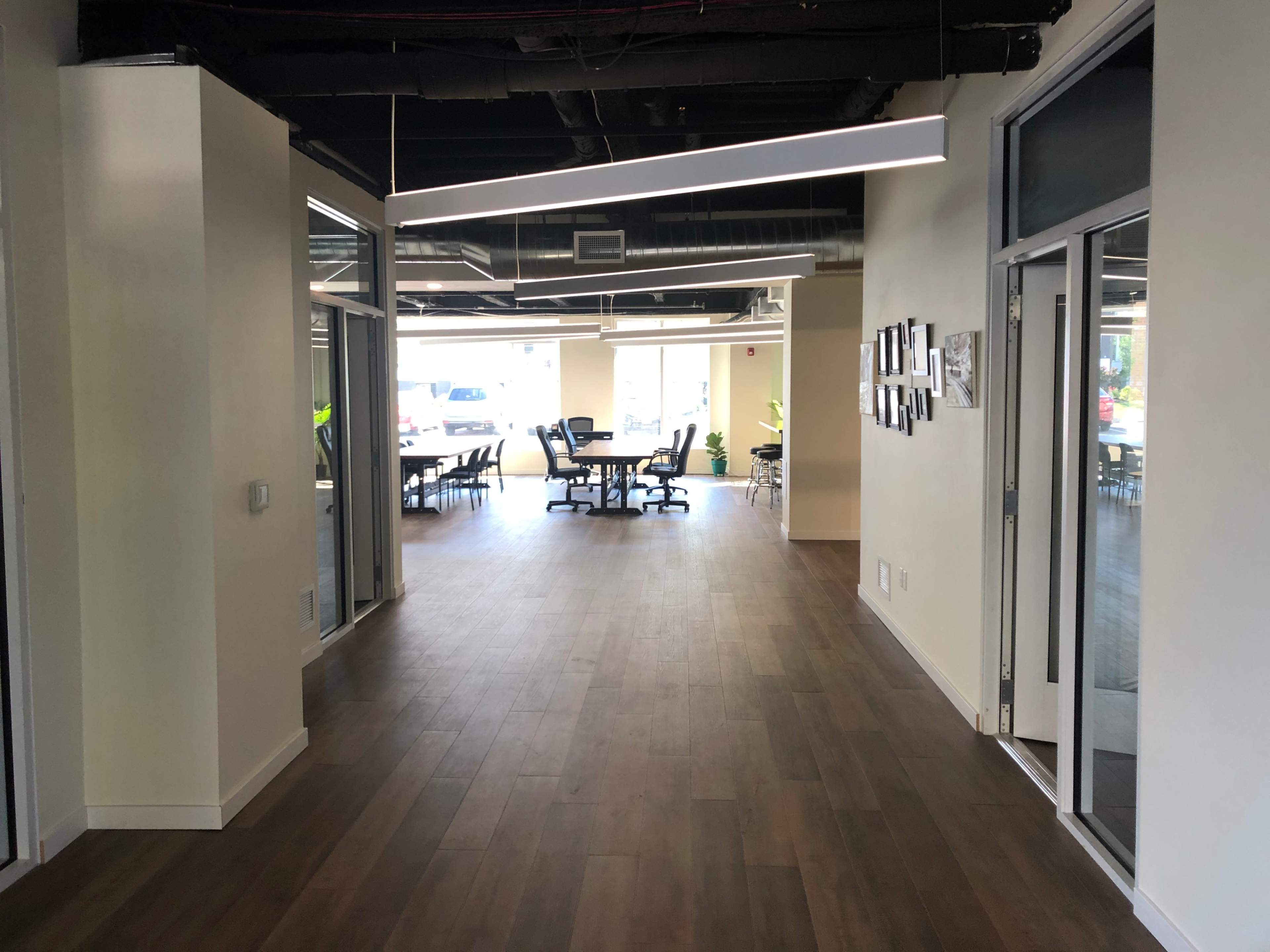 A modern office corridor leading to a conference area with glass walls and wooden flooring.