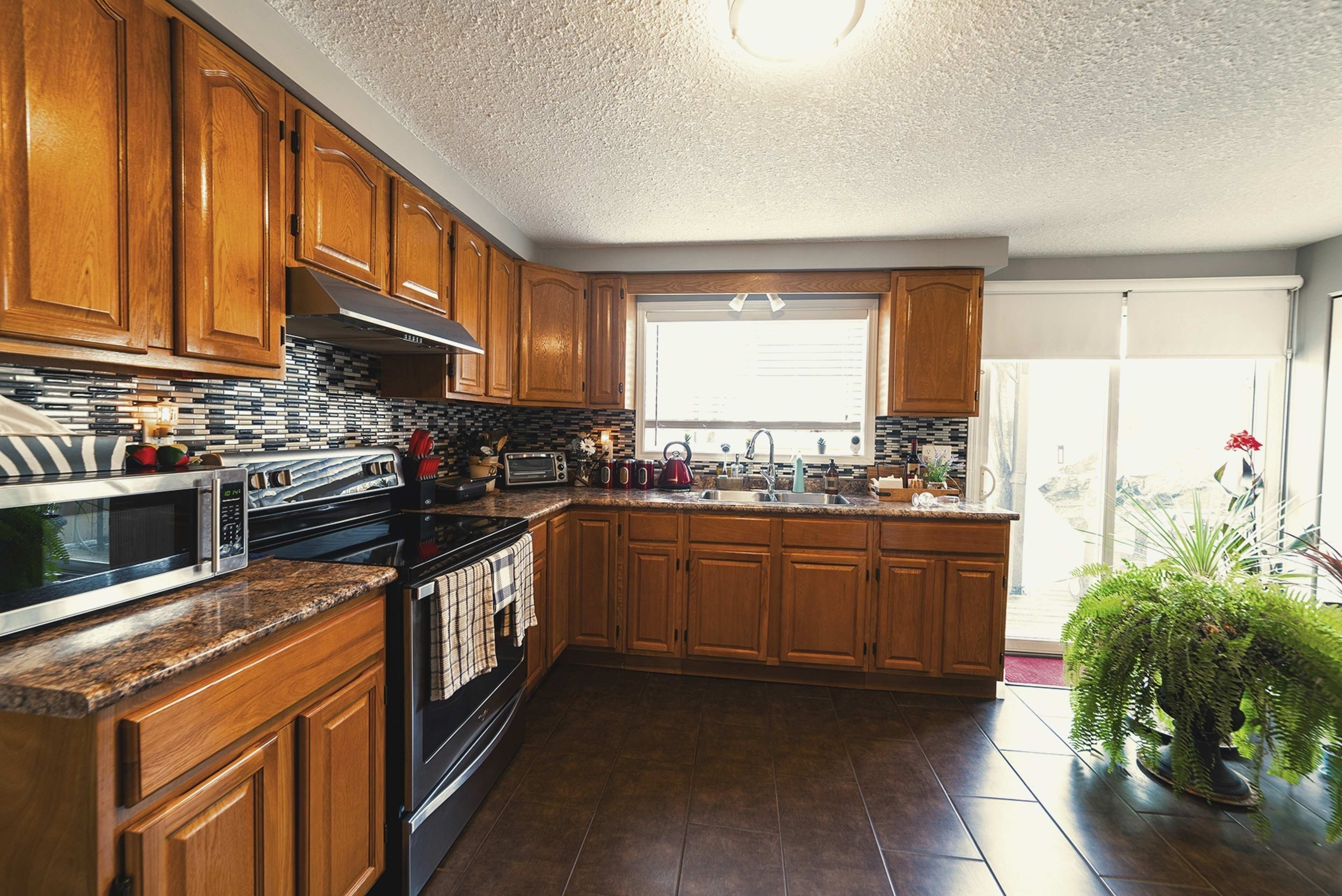 A modern kitchen features wooden cabinets, stainless steel appliances, and a window overlooking an outdoor area.