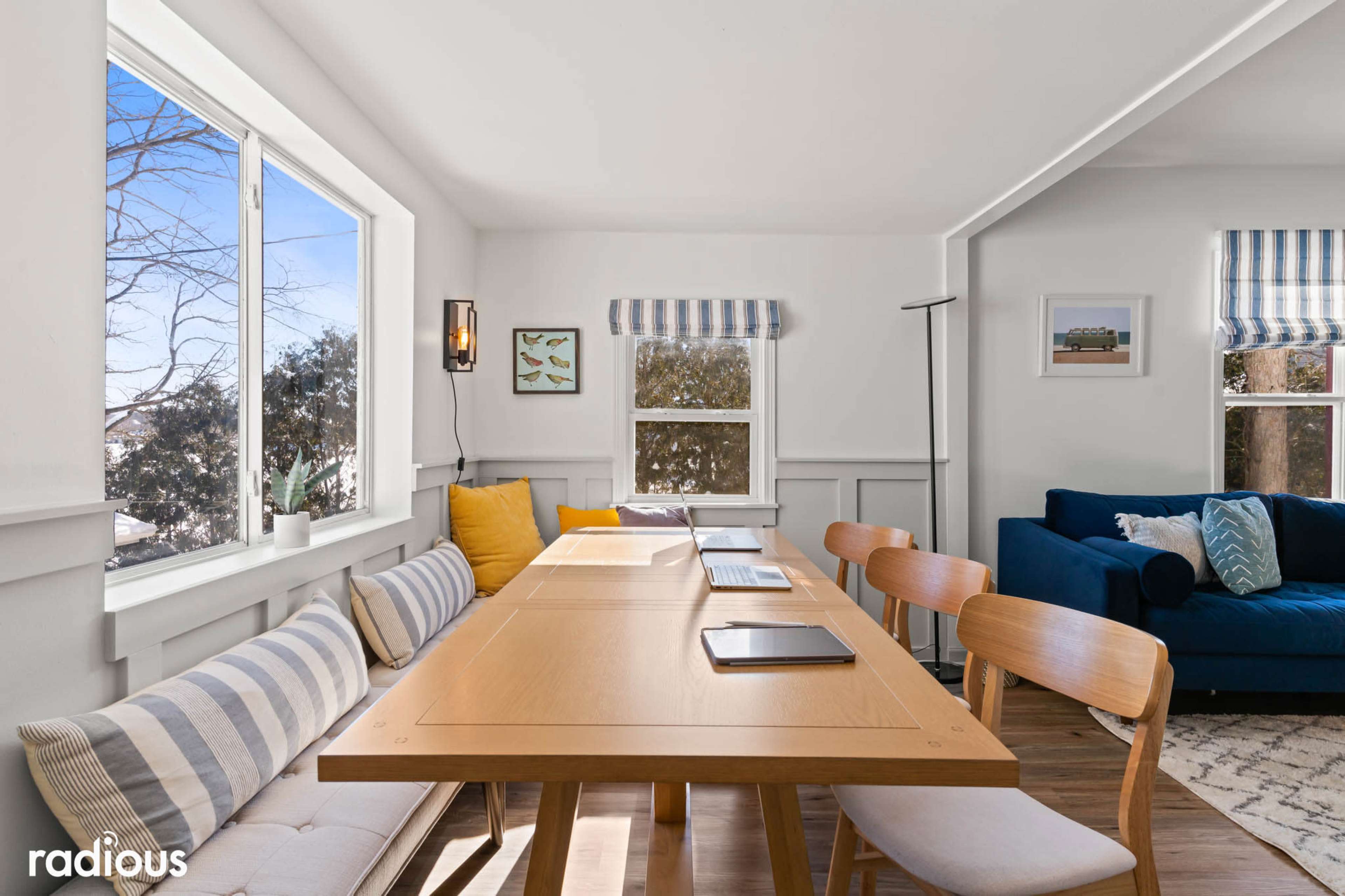 A bright, modern meeting room with a long wooden table, several laptops, and comfortable seating near large windows.