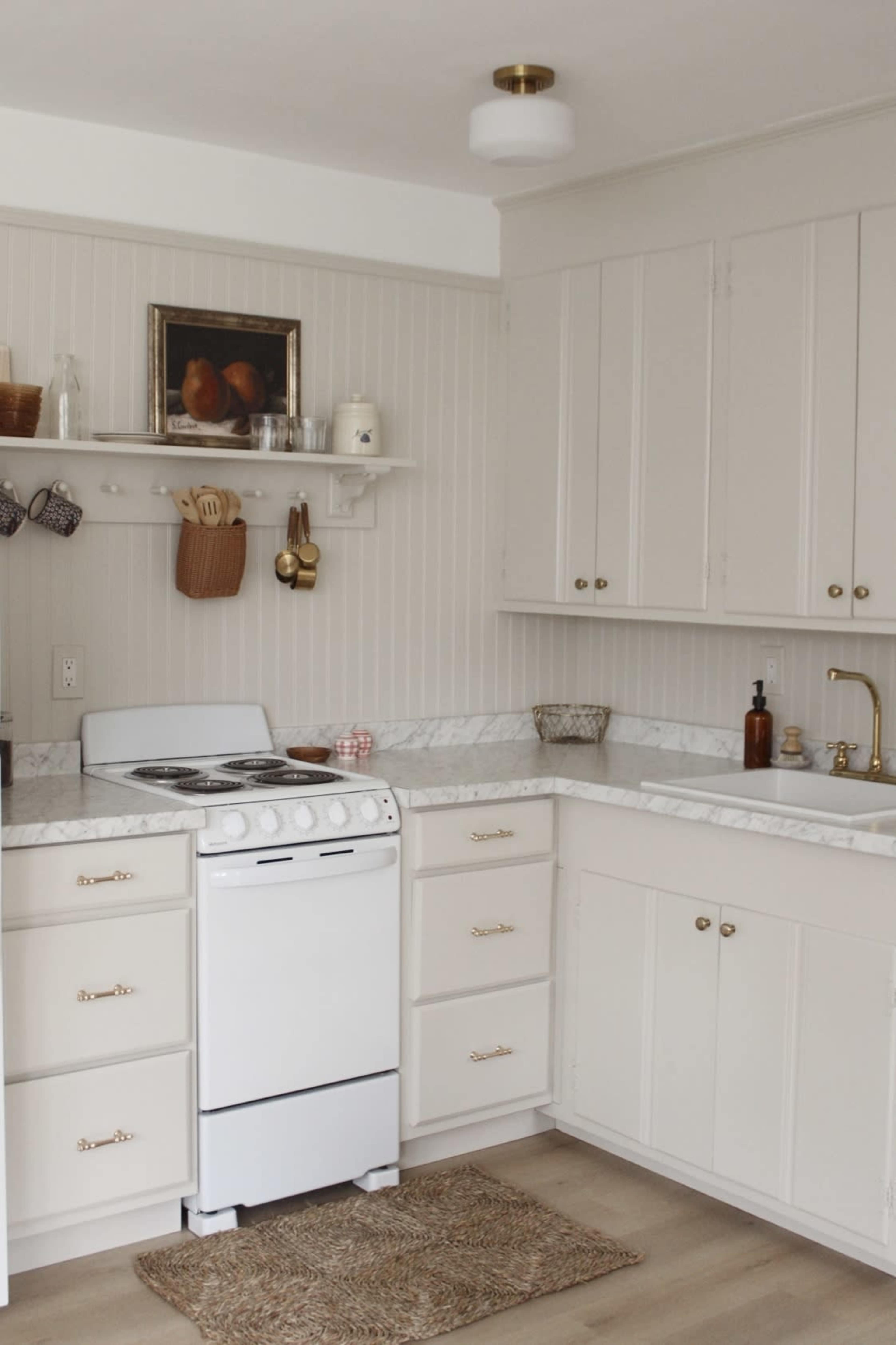 A modern kitchen features white cabinetry, a marble countertop, a small gas stove, and shelves displaying kitchen utensils and decor.