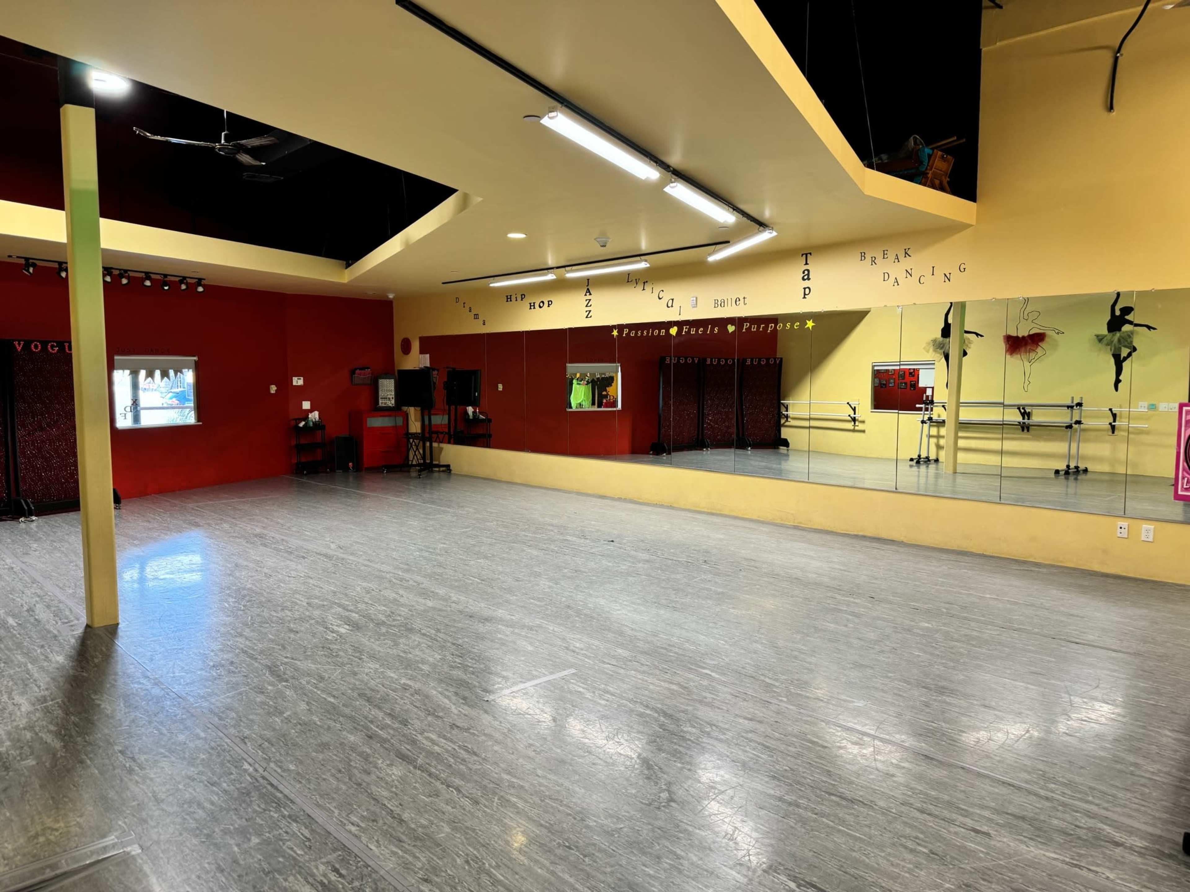 A spacious dance studio with wooden flooring, mirrors along one wall, and colorful painted accents.