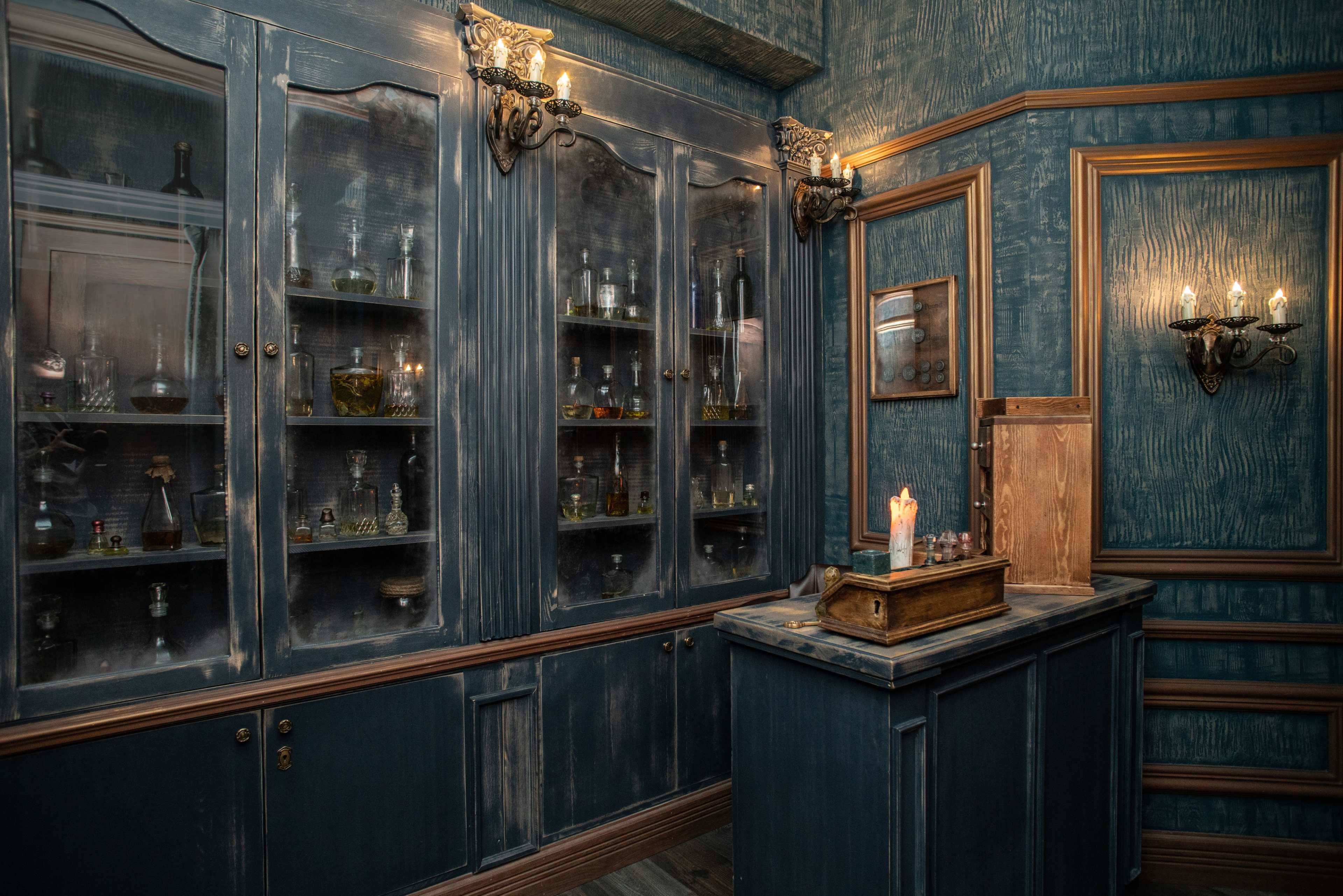 A dimly lit room with dark blue walls, a wooden countertop, a candle, and glass cabinets filled with various bottles and jars.