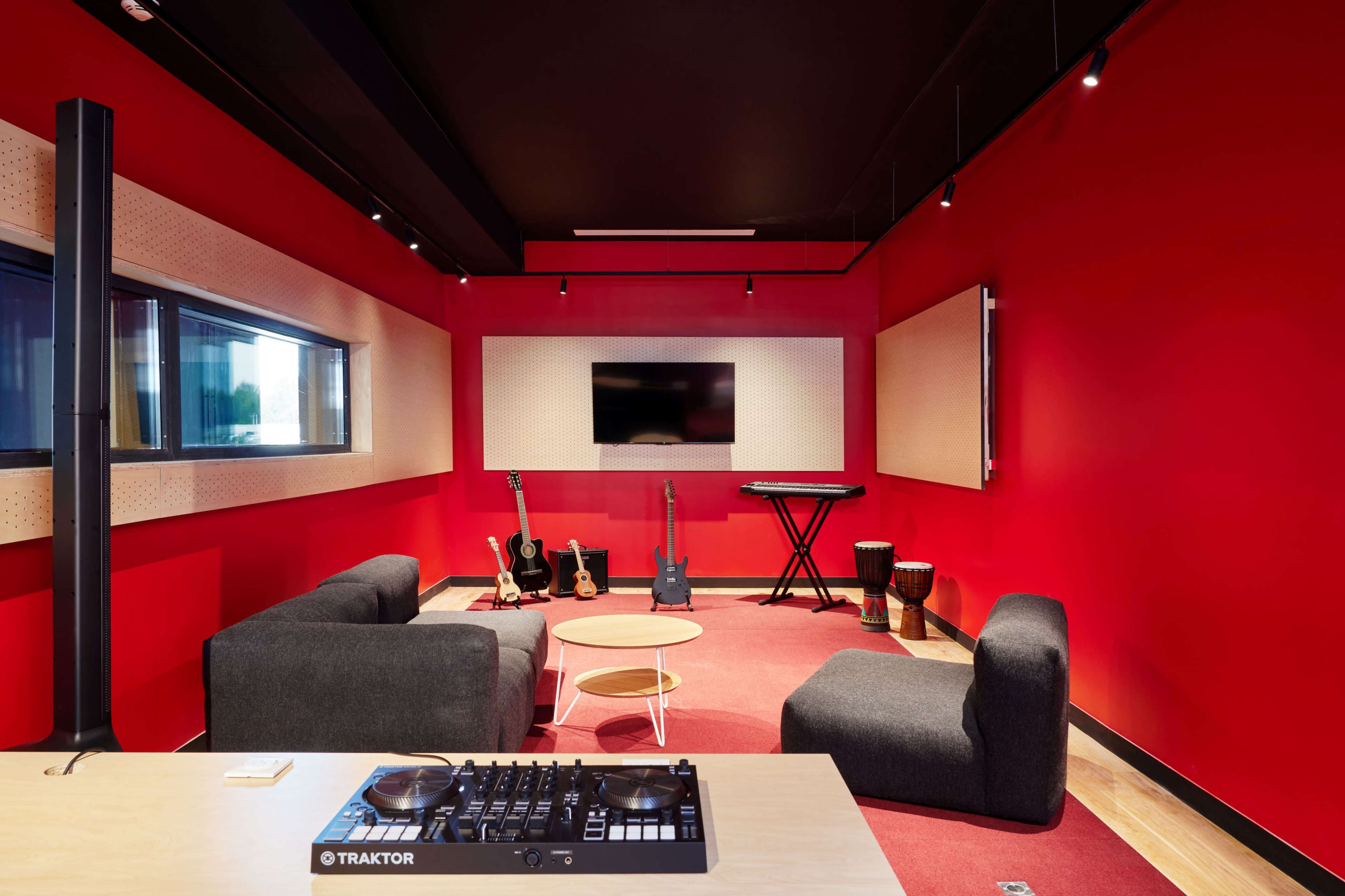 The image features a modern music studio with red walls, a seating area, musical instruments, and a sound mixing console.