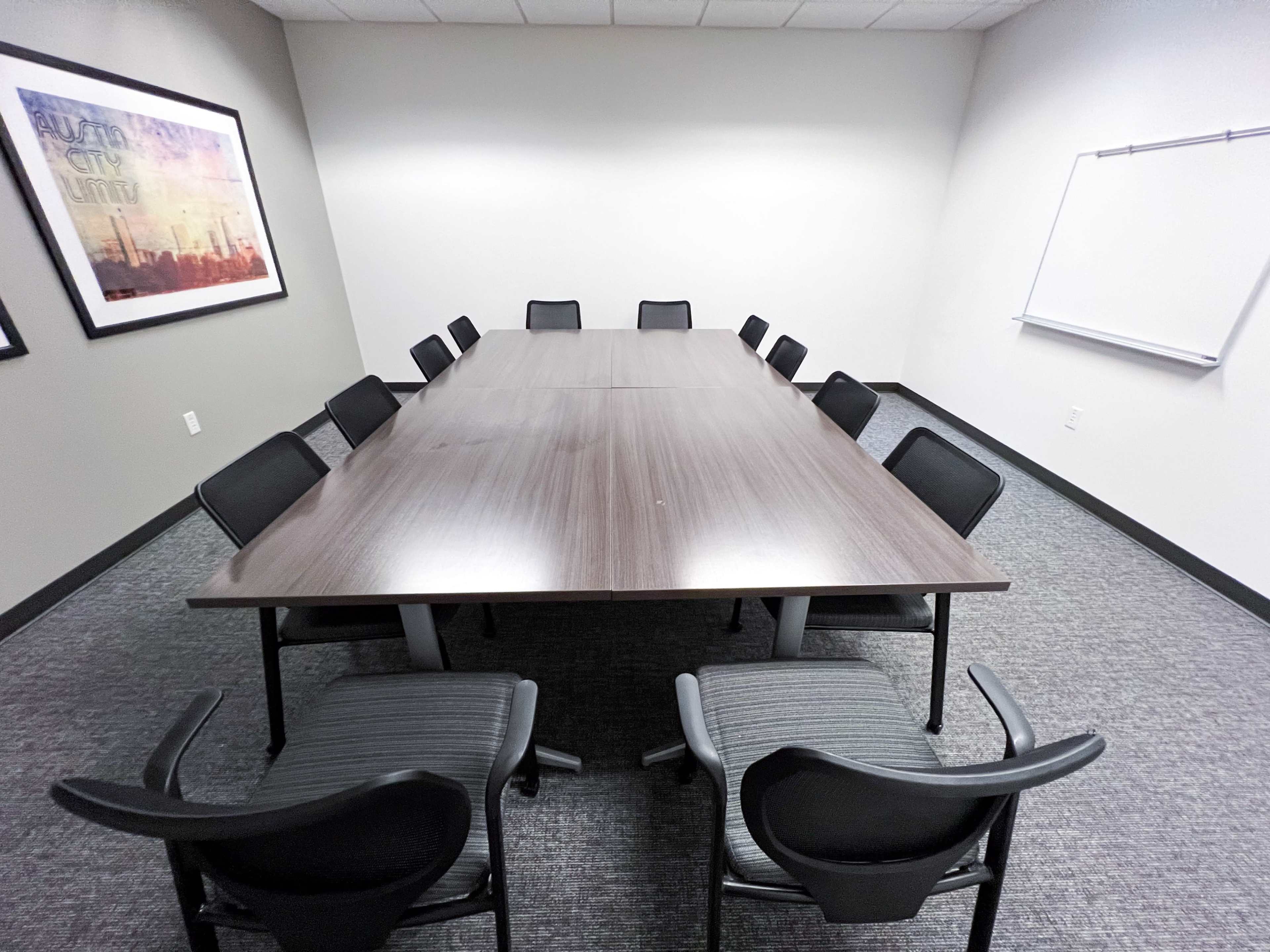 A large, rectangular conference table surrounded by black chairs is set in a sparsely decorated meeting room.