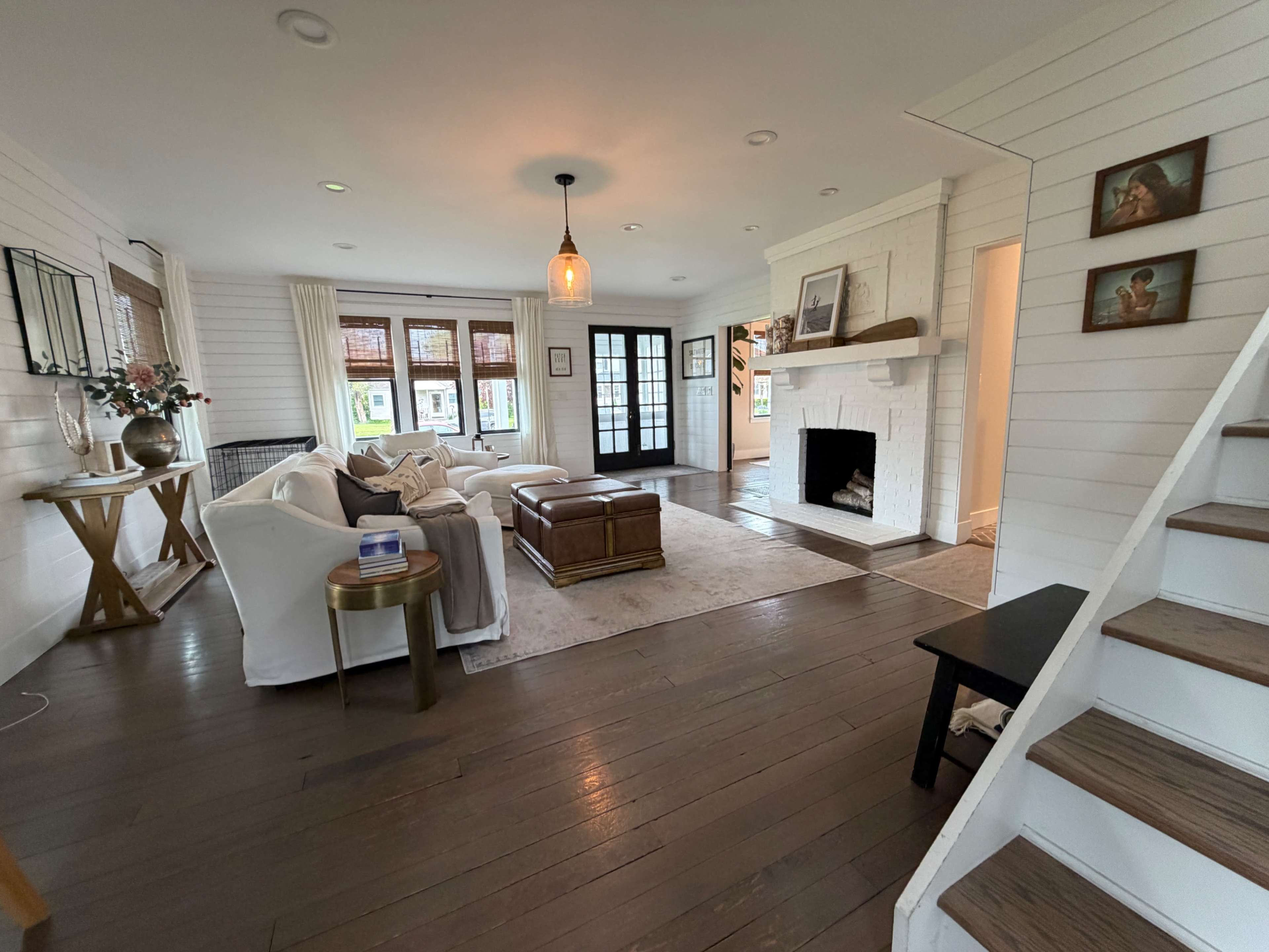 The image shows a cozy living room with white walls, wooden flooring, a fireplace, and a seating area featuring a white couch and a coffee table.