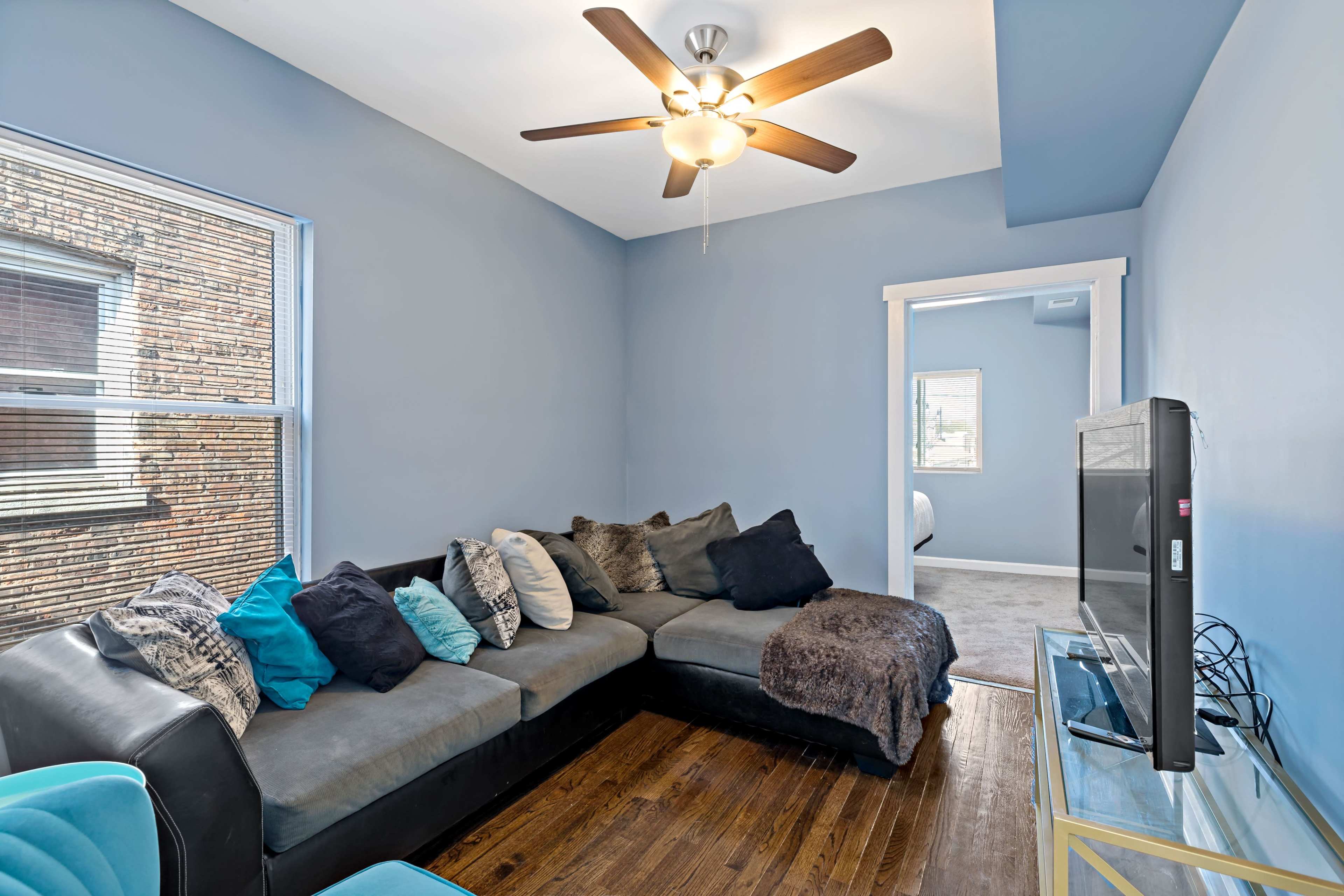 A cozy living room with a sectional sofa adorned with various pillows, a television on a stand, and light blue walls.