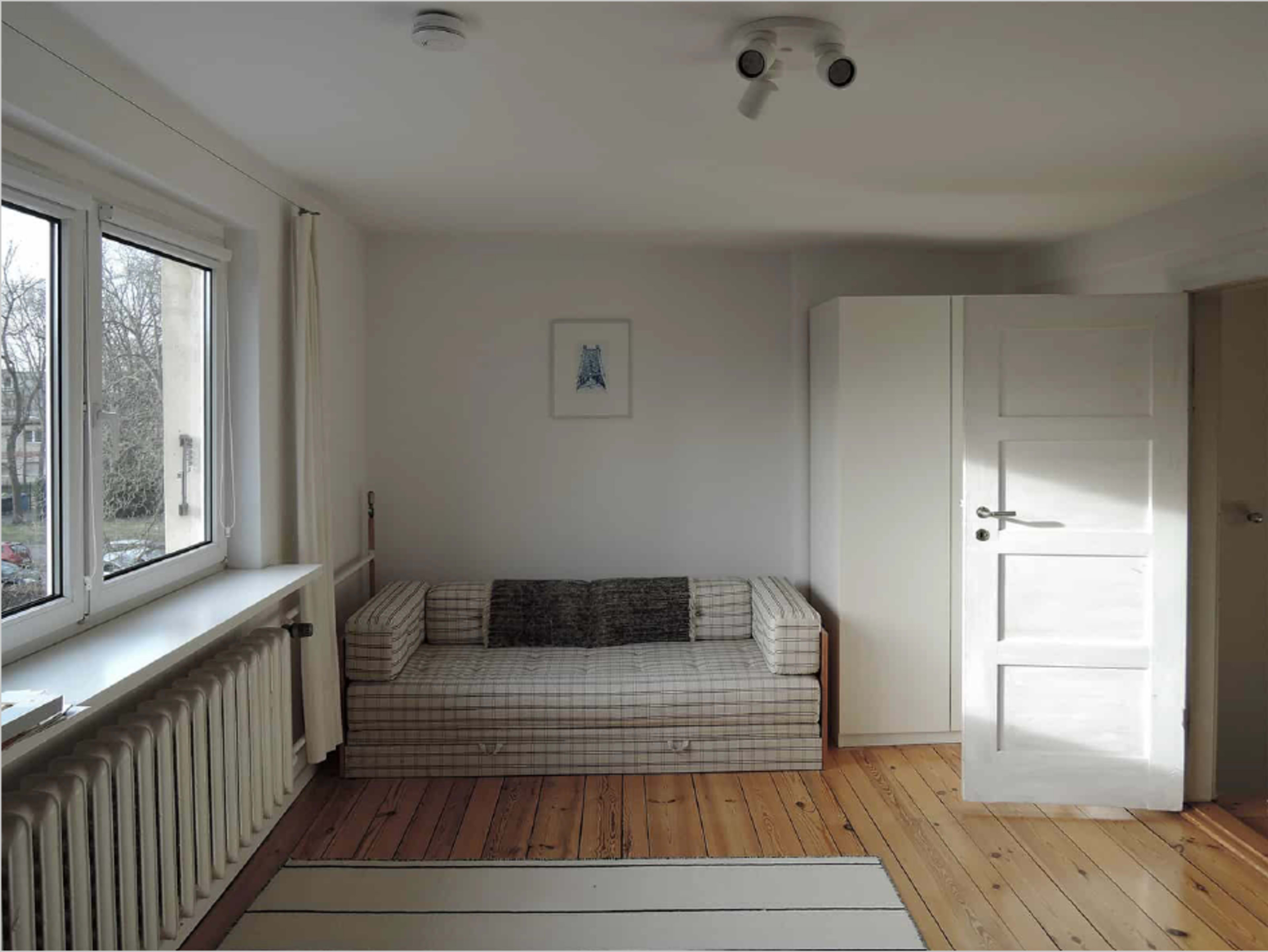 A simple room with a checkered sofa, a radiator, a large window, and a closed white door leading to another space.