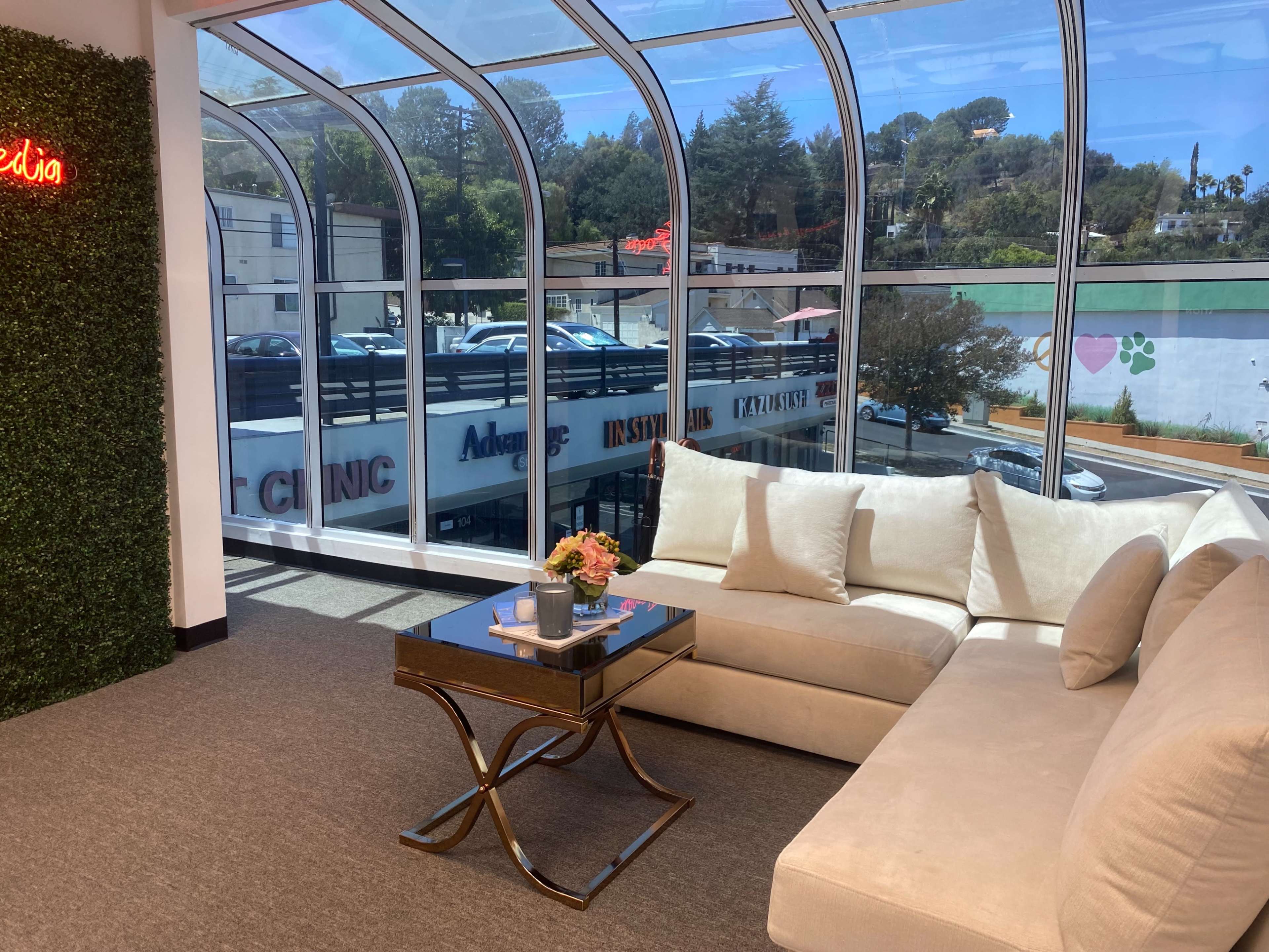 A modern seating area with a large light-colored sofa, a small coffee table, and large windows overlooking a parking lot and nearby buildings.