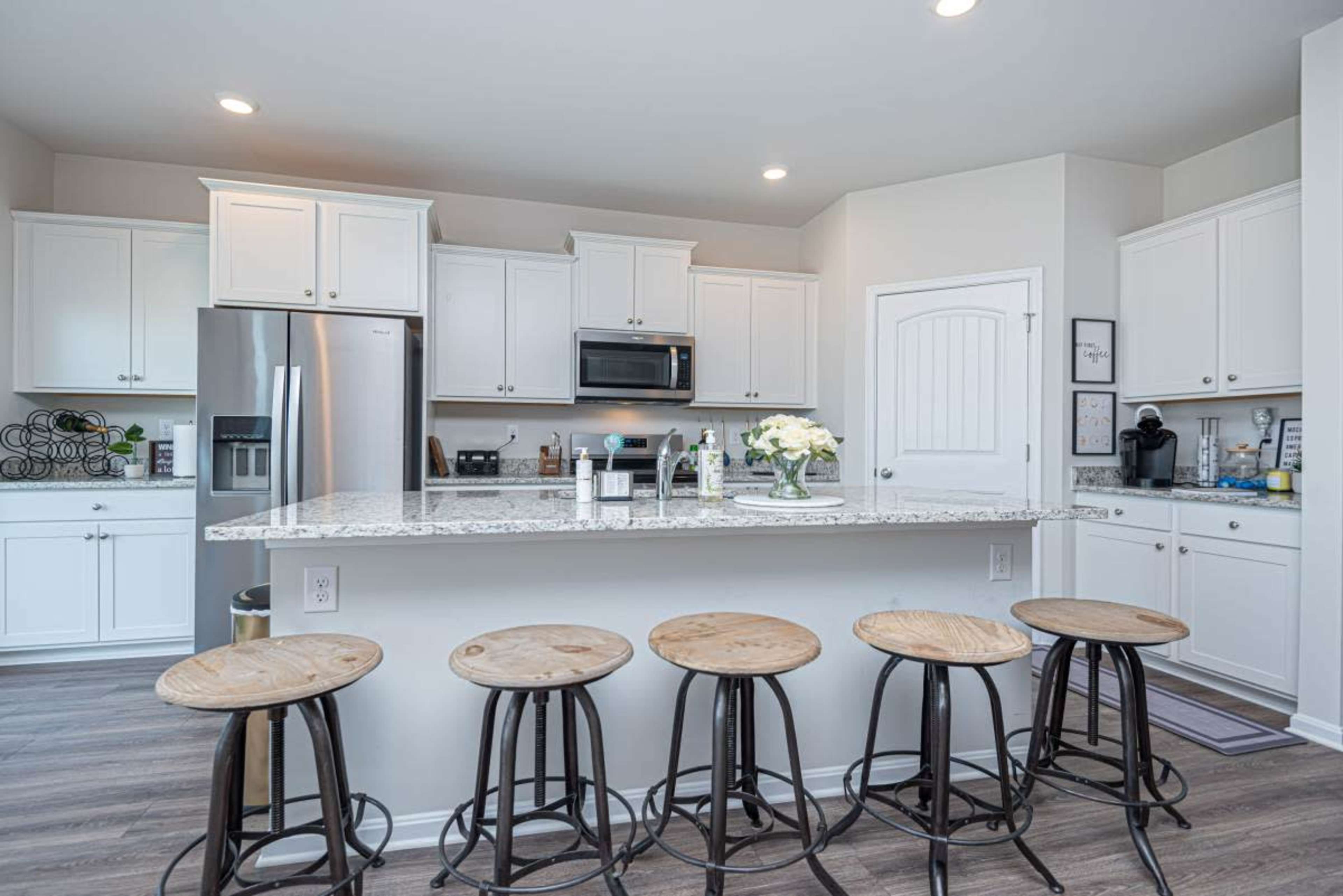 A modern kitchen features white cabinetry, stainless steel appliances, and a central island with five wooden stools.