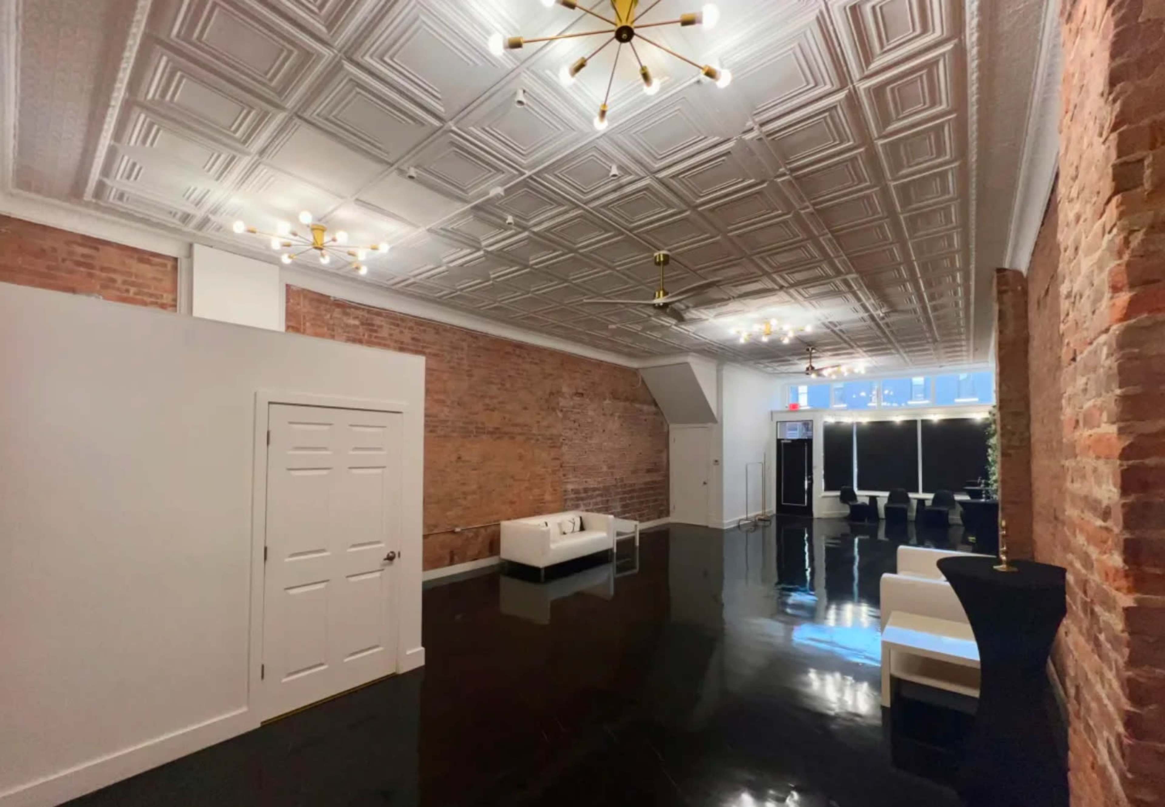 The image shows a spacious interior with exposed brick walls, a glossy black floor, and modern lighting fixtures.