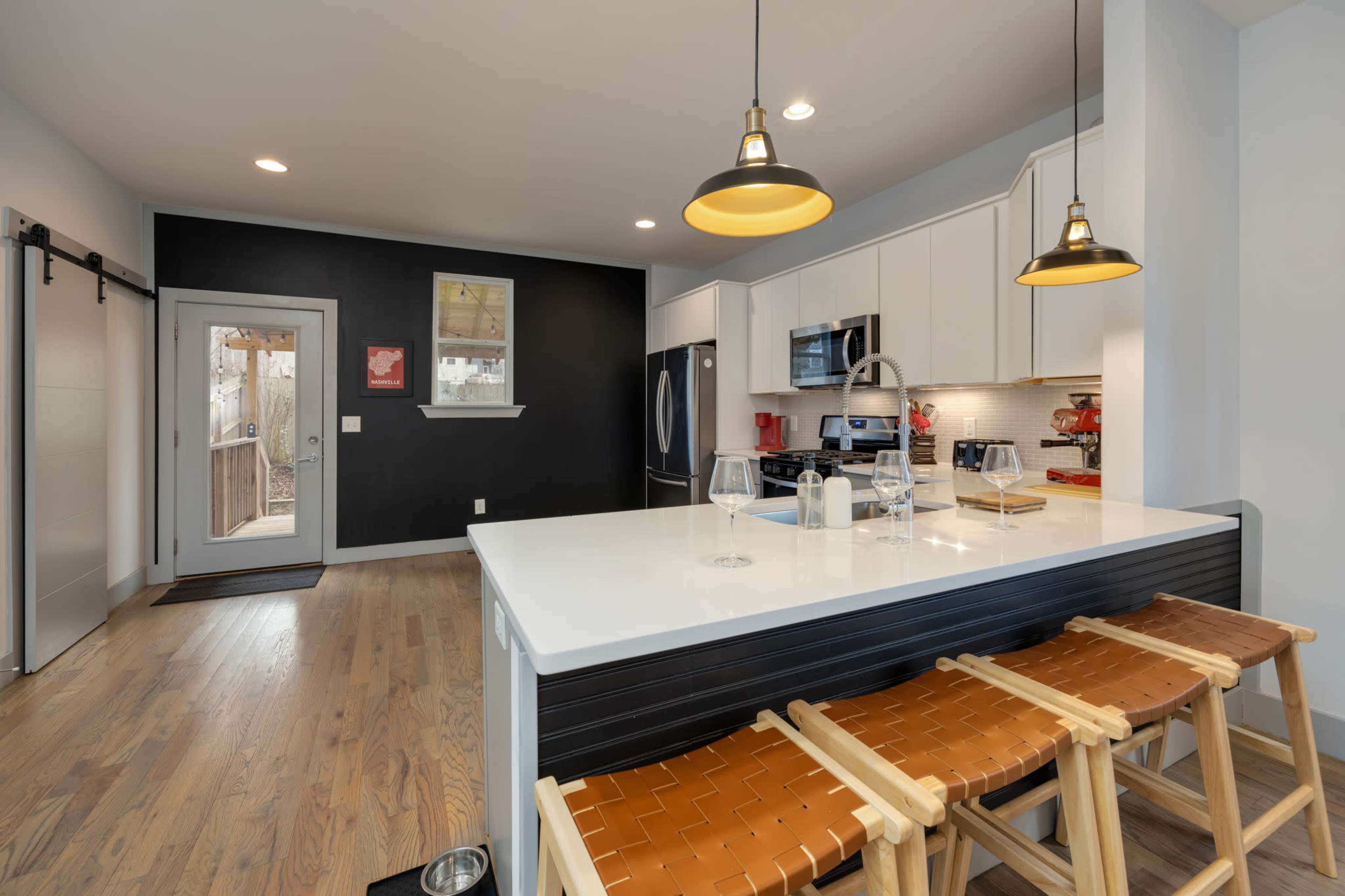 A modern kitchen features a white countertop island with brown bar stools and black cabinetry against a dark wall.