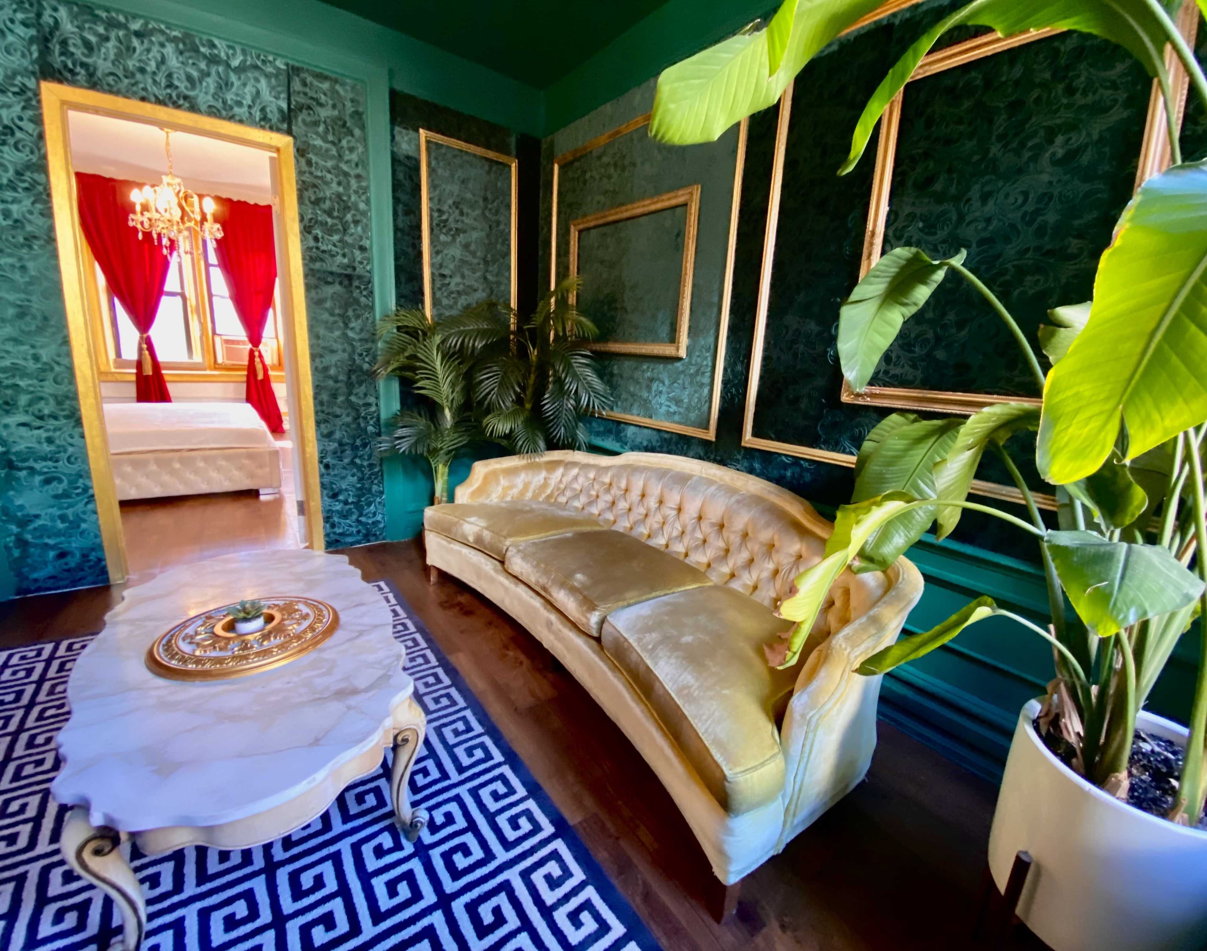 The scene features a luxurious room with a green and gold color scheme, a tufted gold sofa, a round coffee table, a large plant, and a doorway leading to a bedroom with red curtains.